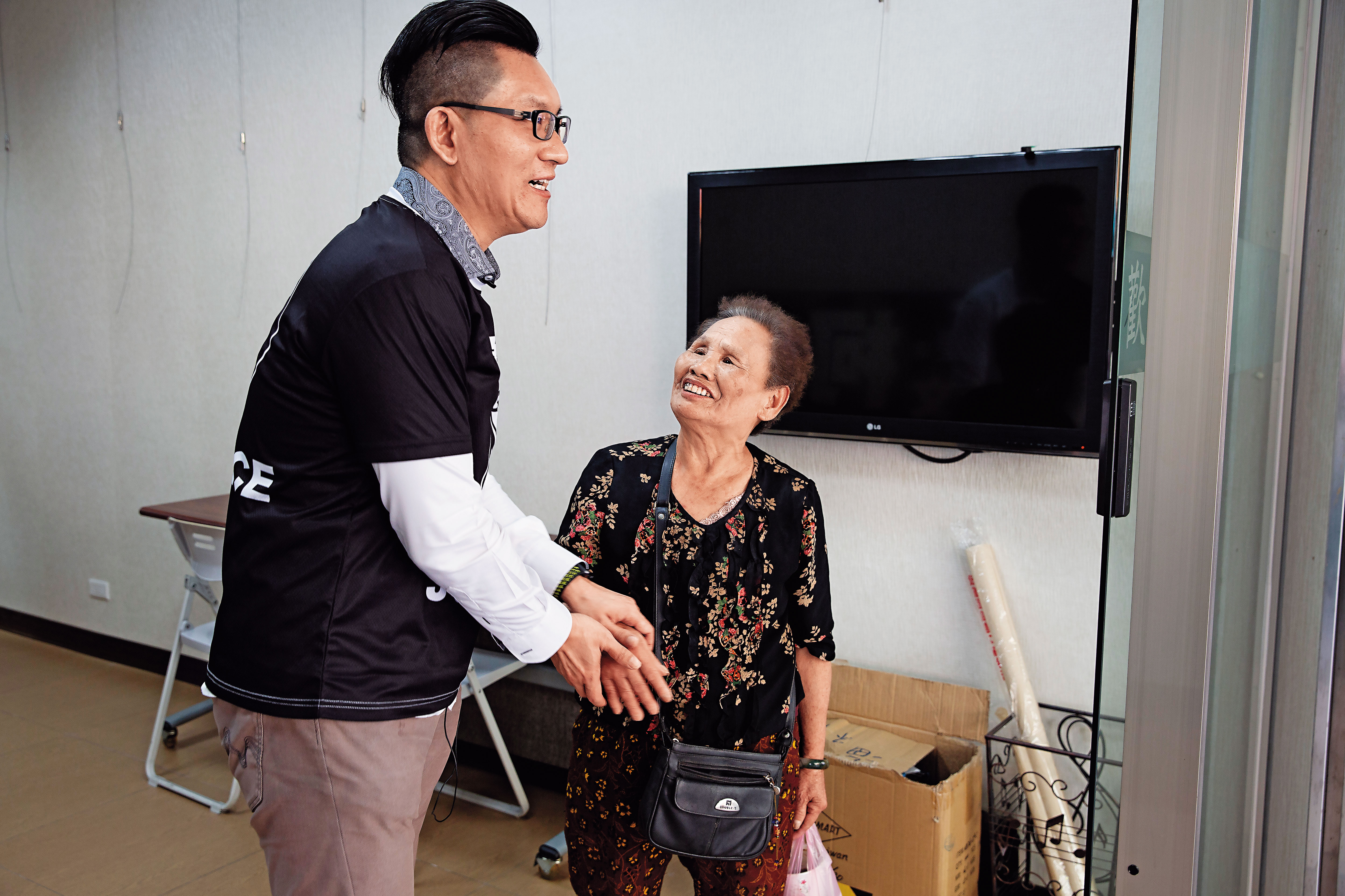 童仲彥(左)轉型當網紅,服務處招牌換裝,一名70歲老婦人搞不清楚狀況,亂入表達支持,還希望他重返政壇、選立委。