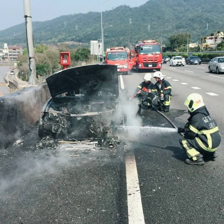 小客車被大火吞噬，消防隊員噴水灌救。（消防局提供）