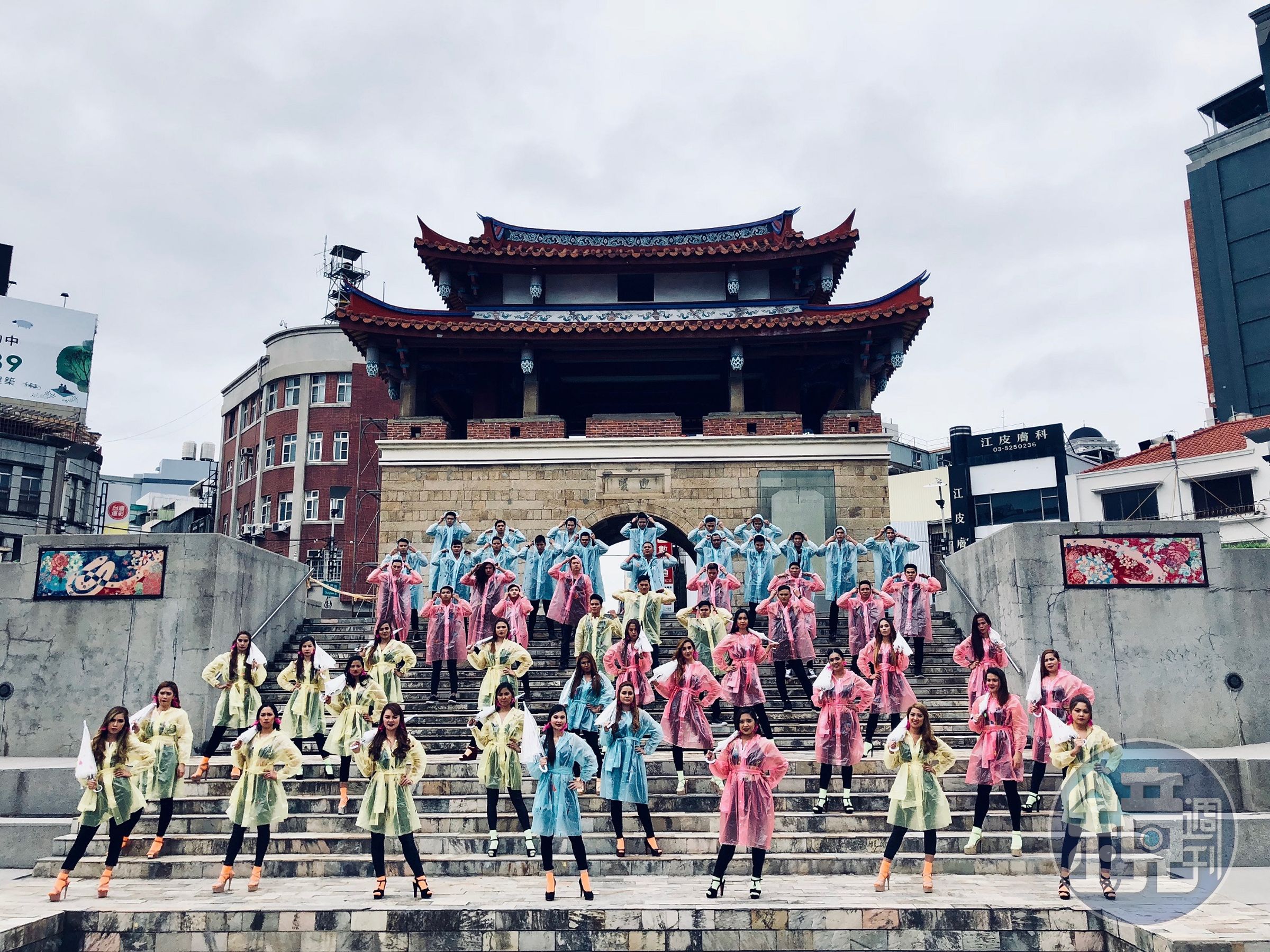 男女共20人的移工，女生拿傘，各自不同顏色的雨衣，展現菲律賓的天氣。