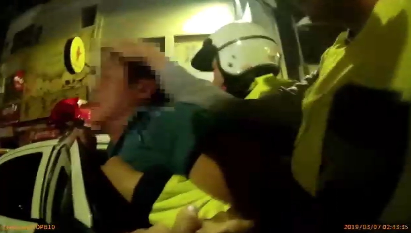 喝得醉醺醺的黃男過馬路遭小黃擦撞，一氣之下痛毆運將，警方將他帶上警車。（警方提供）