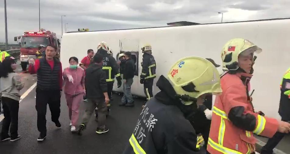救護人員從翻覆的遊覽車頂逃生口,救出受困及受傷的乘客。(翻攝畫面)