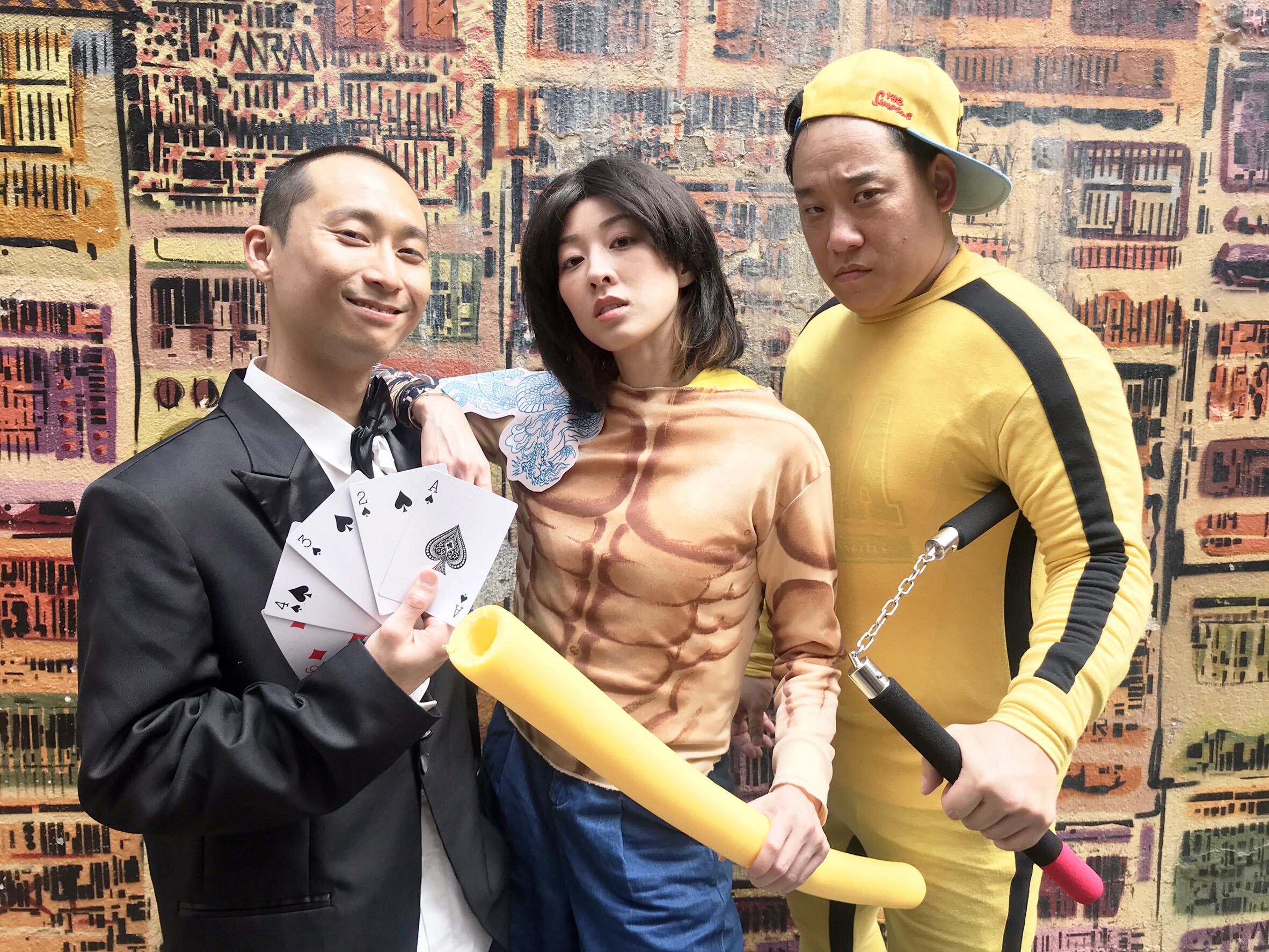 浩子（左）扮成「周潤發-賭神」，夏語心（中）扮成「銅鑼灣扛霸子－陳浩南」，阿龐則打扮成「李小龍」，一行人去中環壁畫打卡熱點「九龍城寨」拍照。（民視提供）