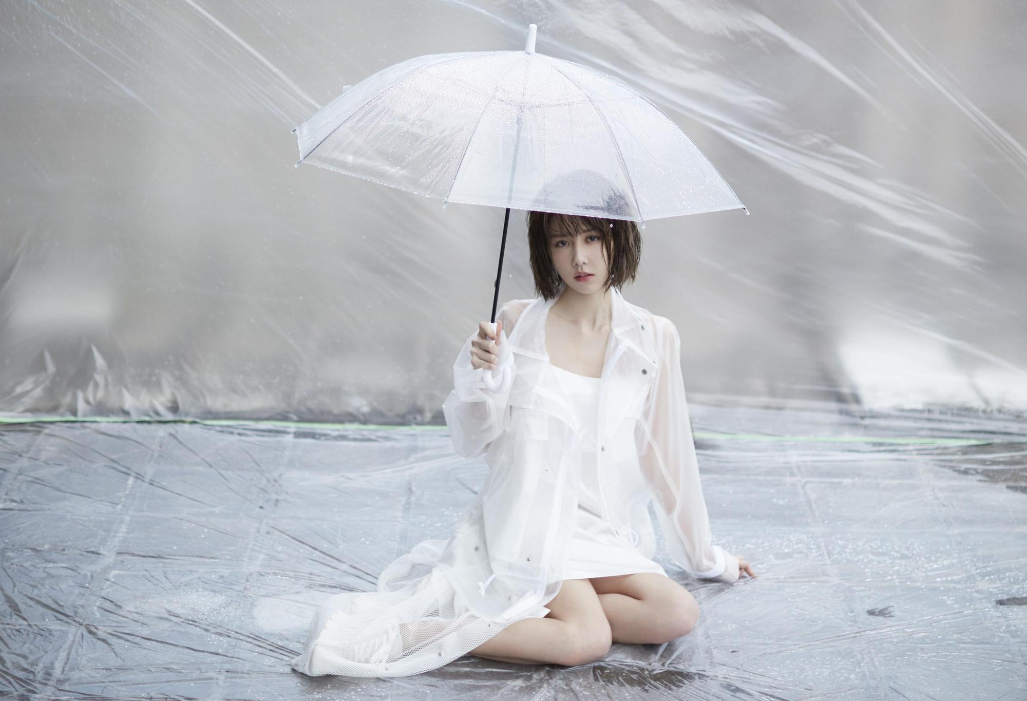 邵雨薇穿著白色透明雨衣洋裝,撐著雨傘趴在炙熱的柏油路上。(寬宏藝術Kham Music)