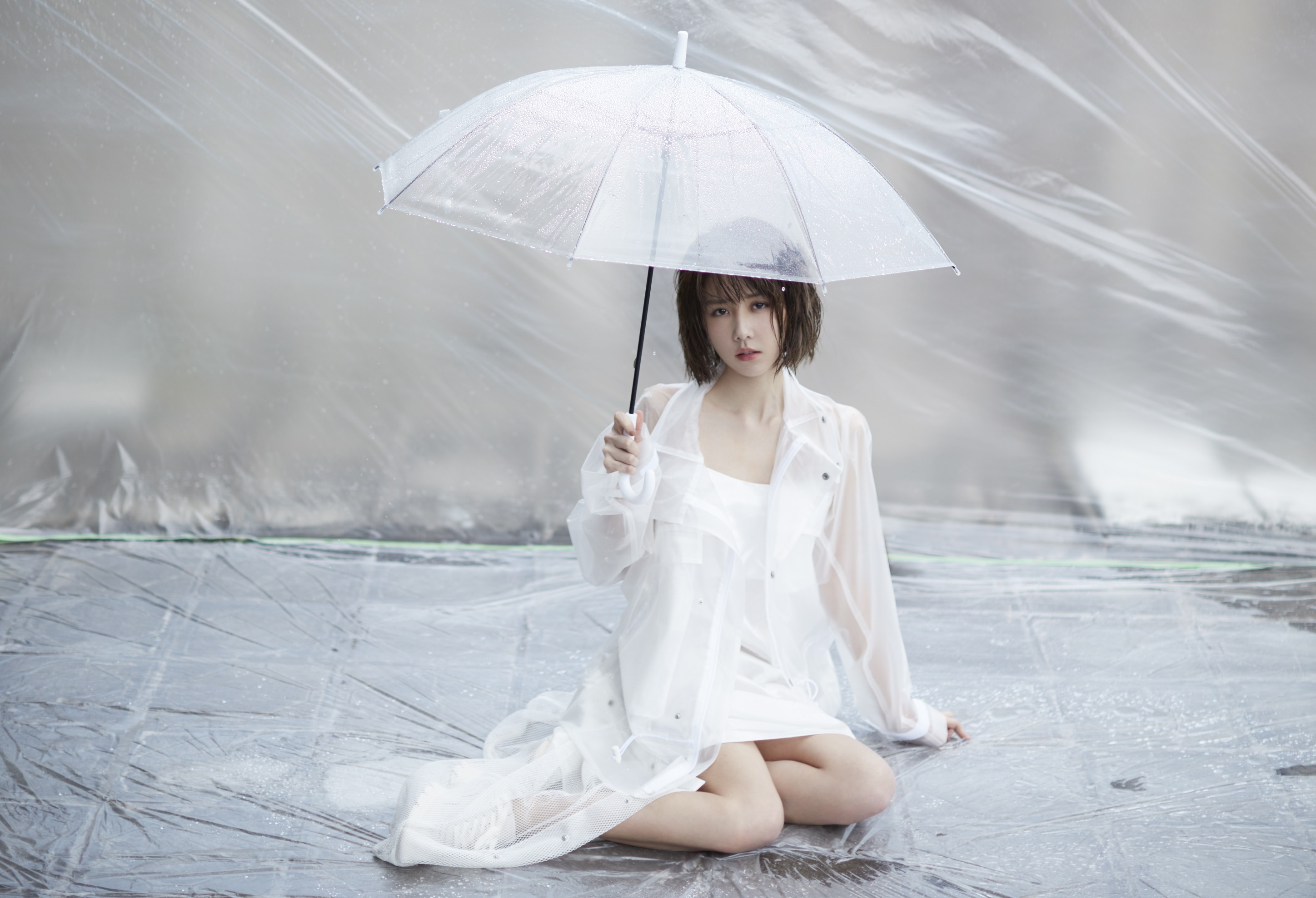 邵雨薇穿著白色透明雨衣洋裝，撐著雨傘趴在炙熱的柏油路上。（寬宏藝術Kham Music）