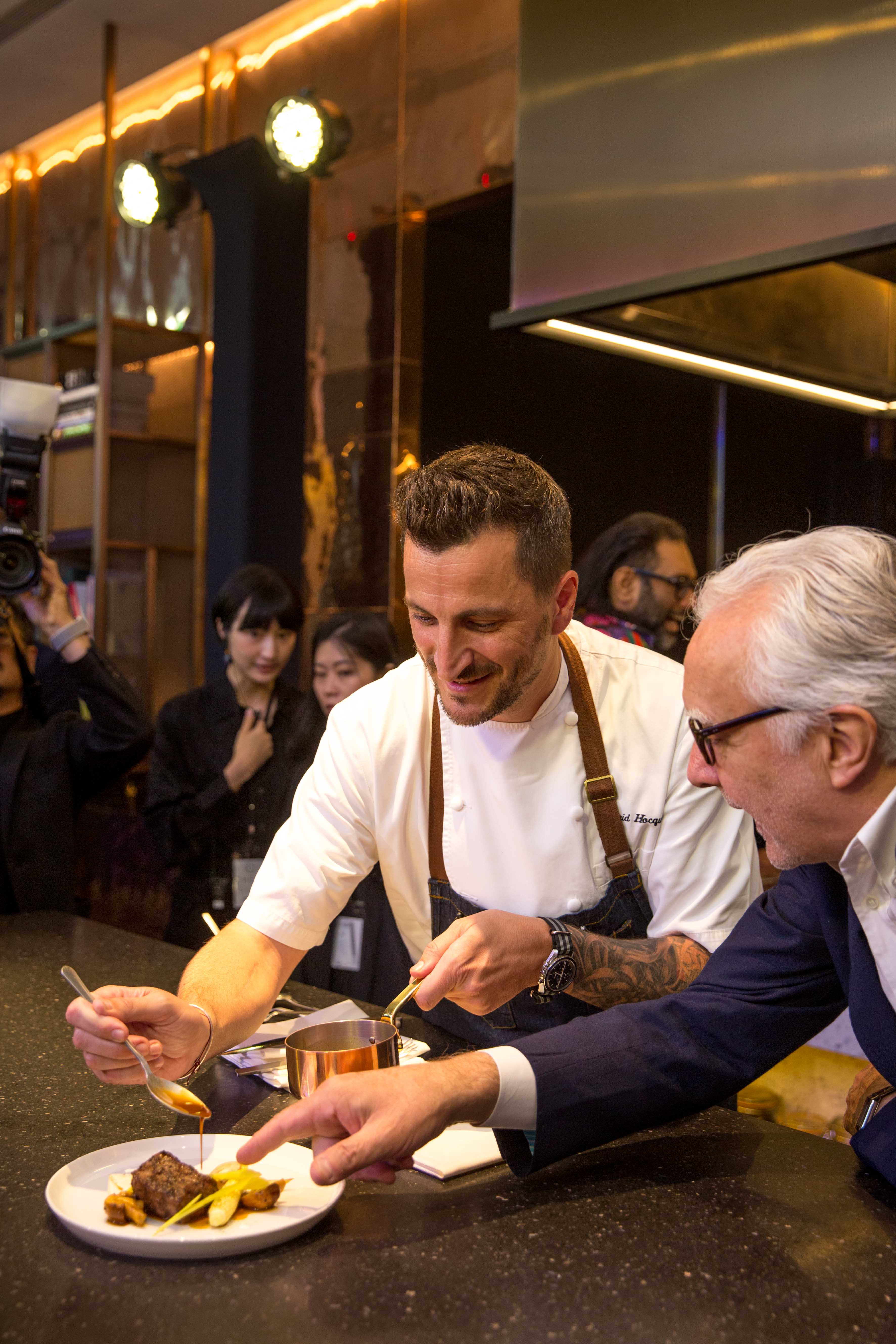 「Chefs Club Taipei」首位客座主廚Wilfrid Hocquet（左）展演菜色時，師父杜卡斯（右）在旁指點。