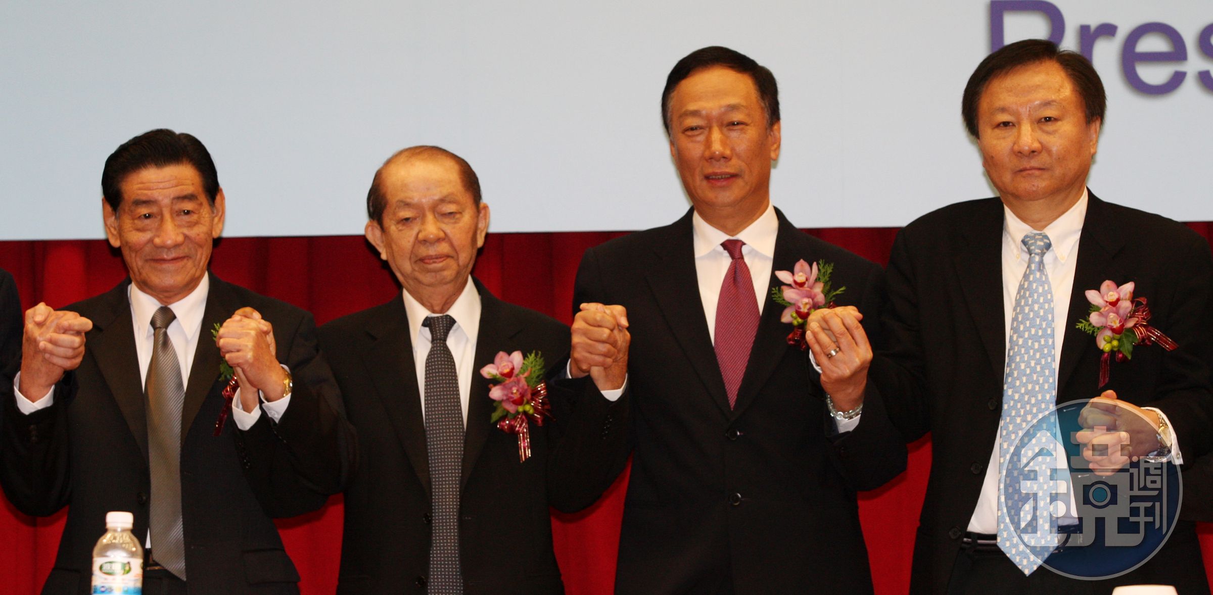 2009年鴻海董事長郭台銘（右2）手牽奇美創辦人許文龍（左2），宣布奇美電與群創光電合併。（中央社）