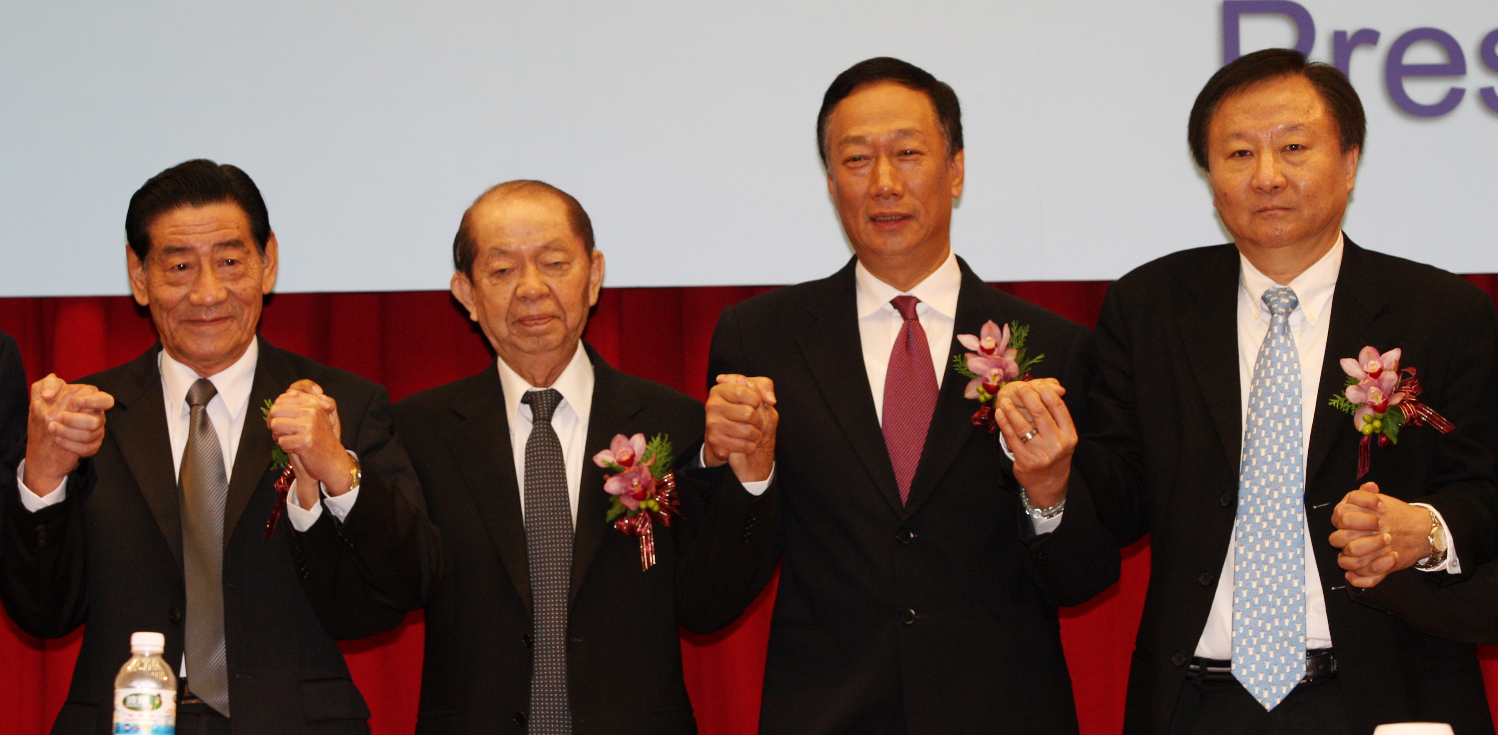 2009年鴻海董事長郭台銘（右2）手牽奇美創辦人許文龍（左2），宣布奇美電與群創光電合併。（中央社）