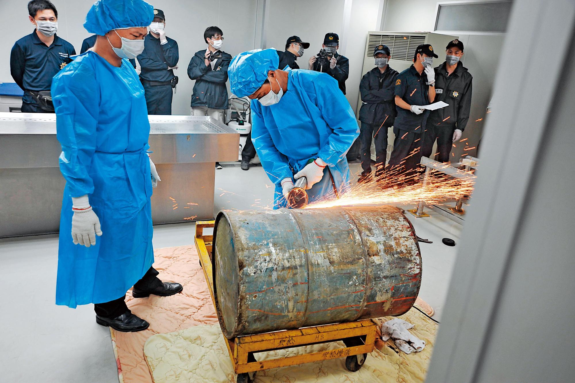 檢警人員戴著口罩在殯儀館內,利用砂輪機等工具將陳文軒遺體從汽油桶內取出。