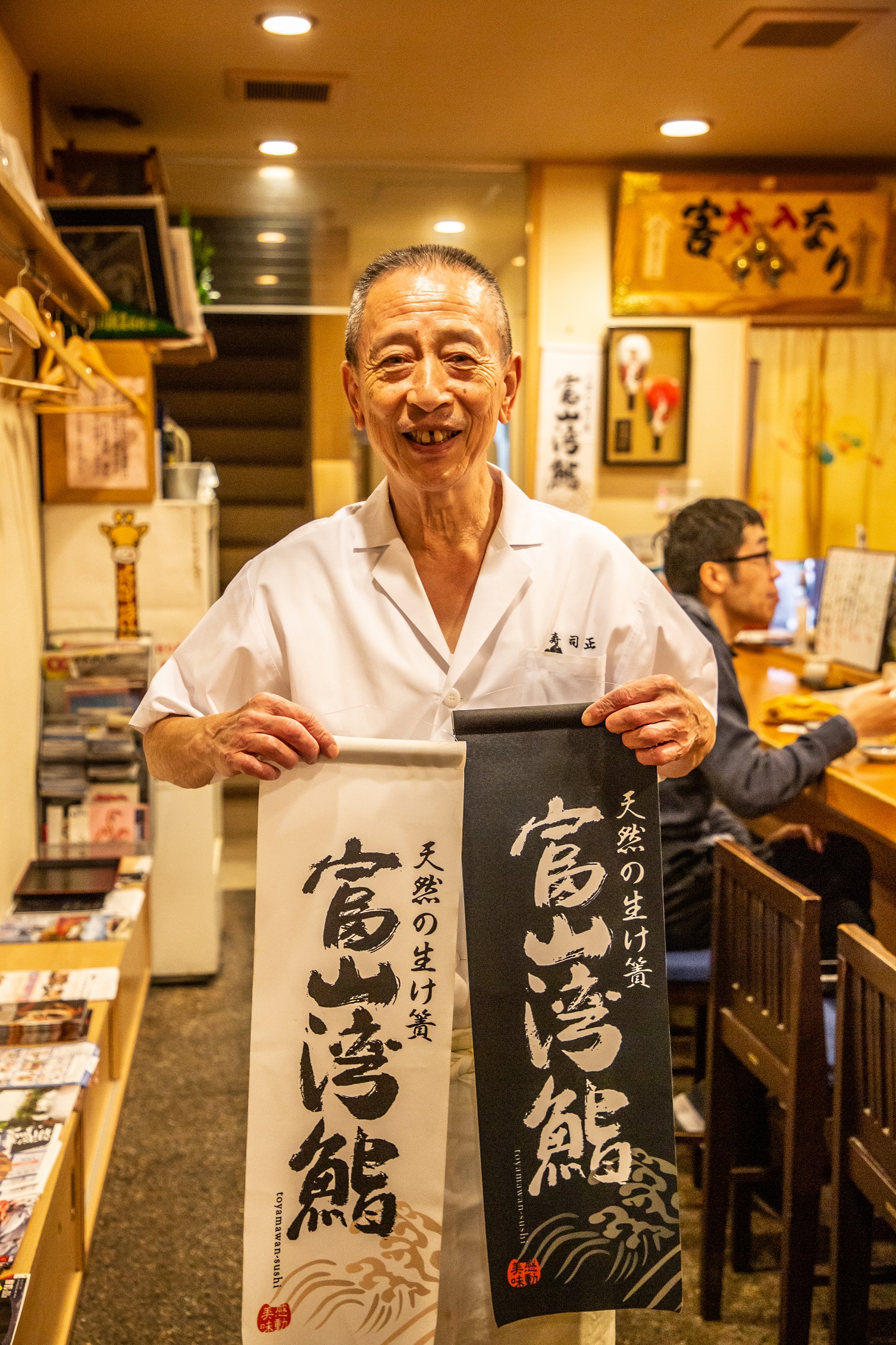 「江戶前壽司正」老闆熱情拿著印有「富山灣鮨」的掛旗。