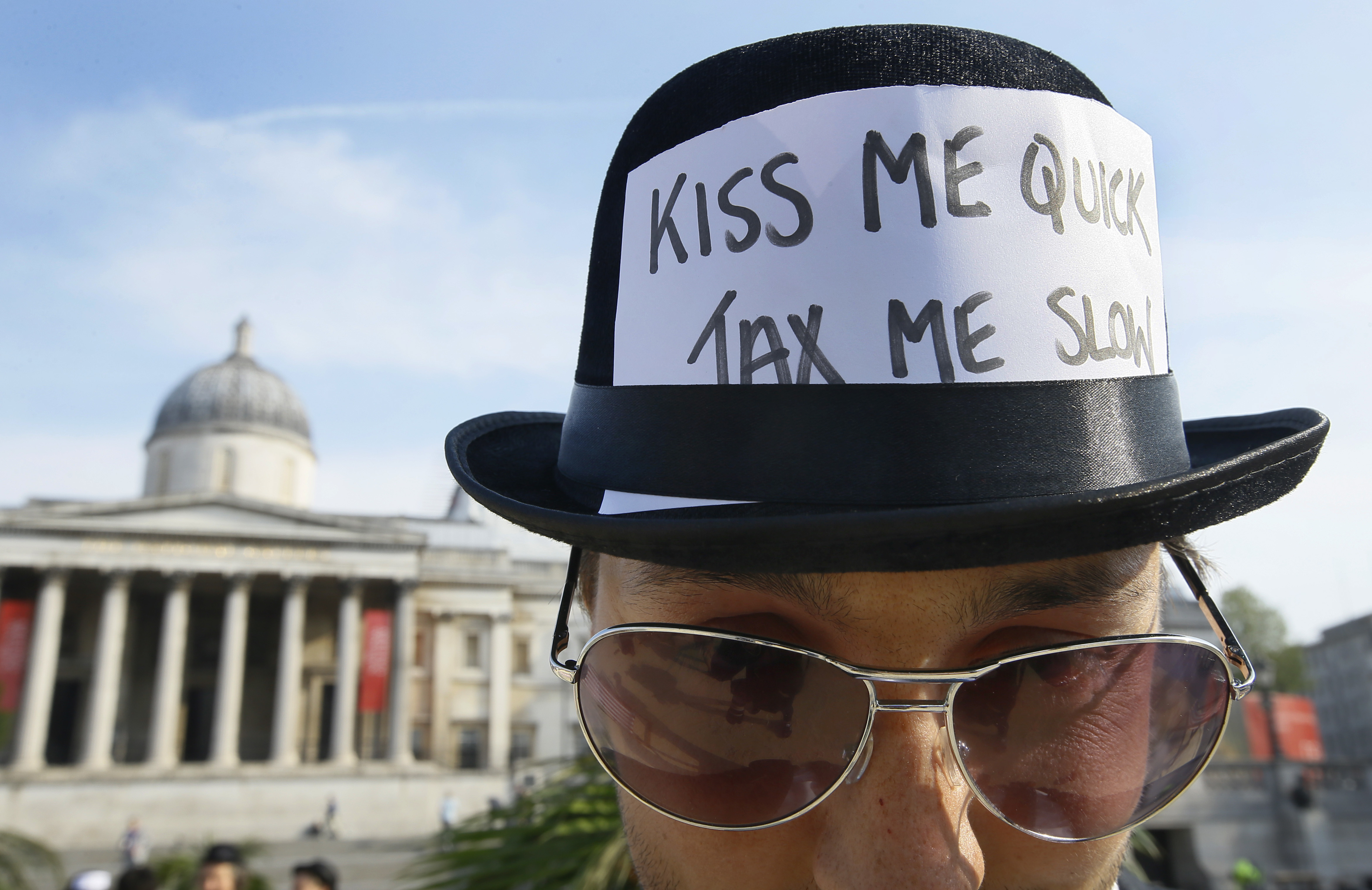 英國倫敦「反腐高峰會」的抗議民眾,頭上帽子的標語寫著「吻我就搶快,課稅慢慢來」(東方IC)