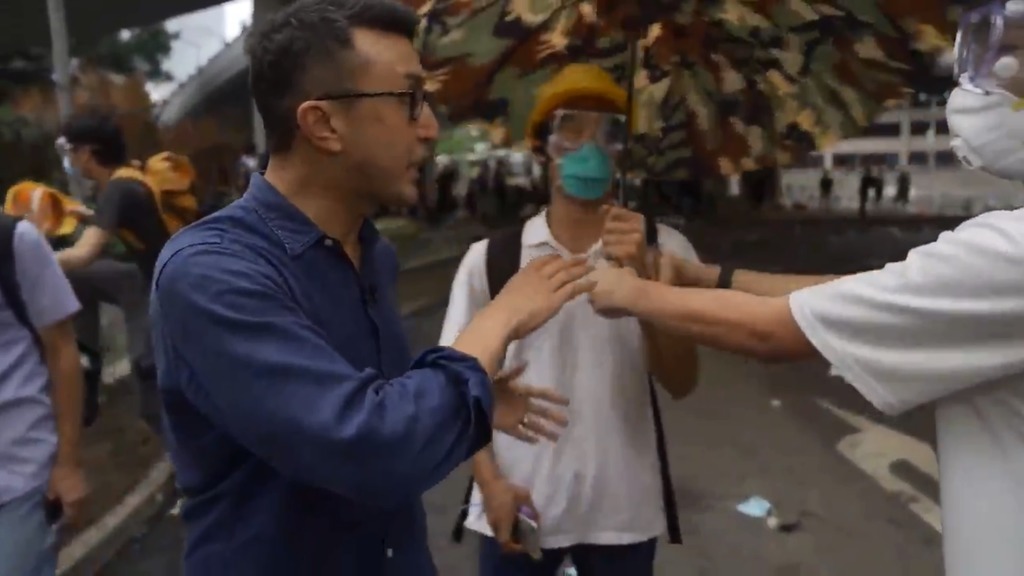 一名美國CBS電視台記者在前線報導時，身上沒有帶任何防護配備，示威者見狀送上雨傘和頭盔。（翻攝Ramy Inocencio推特）