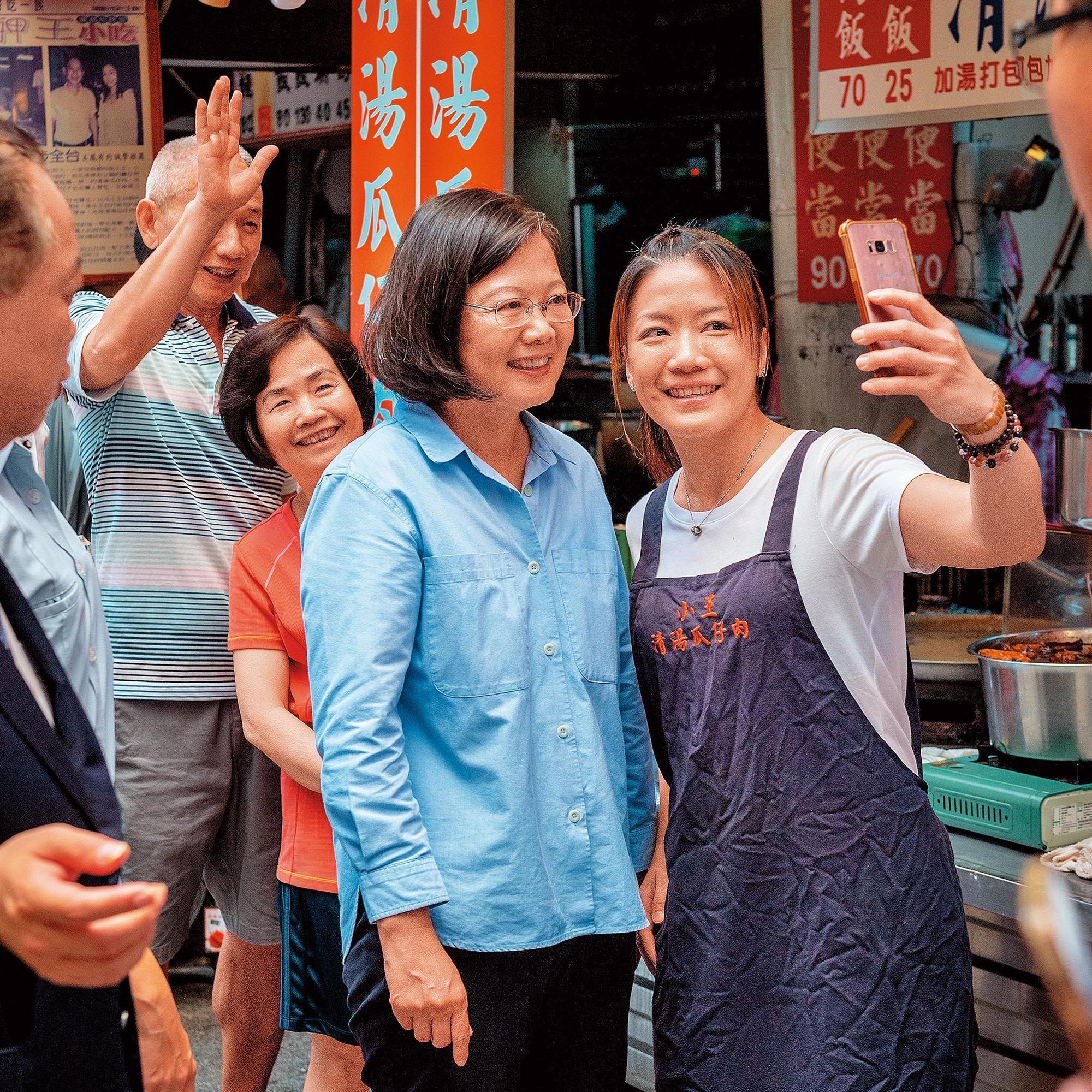 蔡英文(前左)在初選期間成功塑造「辣台妹」形象,支持度回溫,圖為蔡英文16日走訪台北萬華華西街,熱情攤商拿出手機與蔡自拍。(總統府提供)