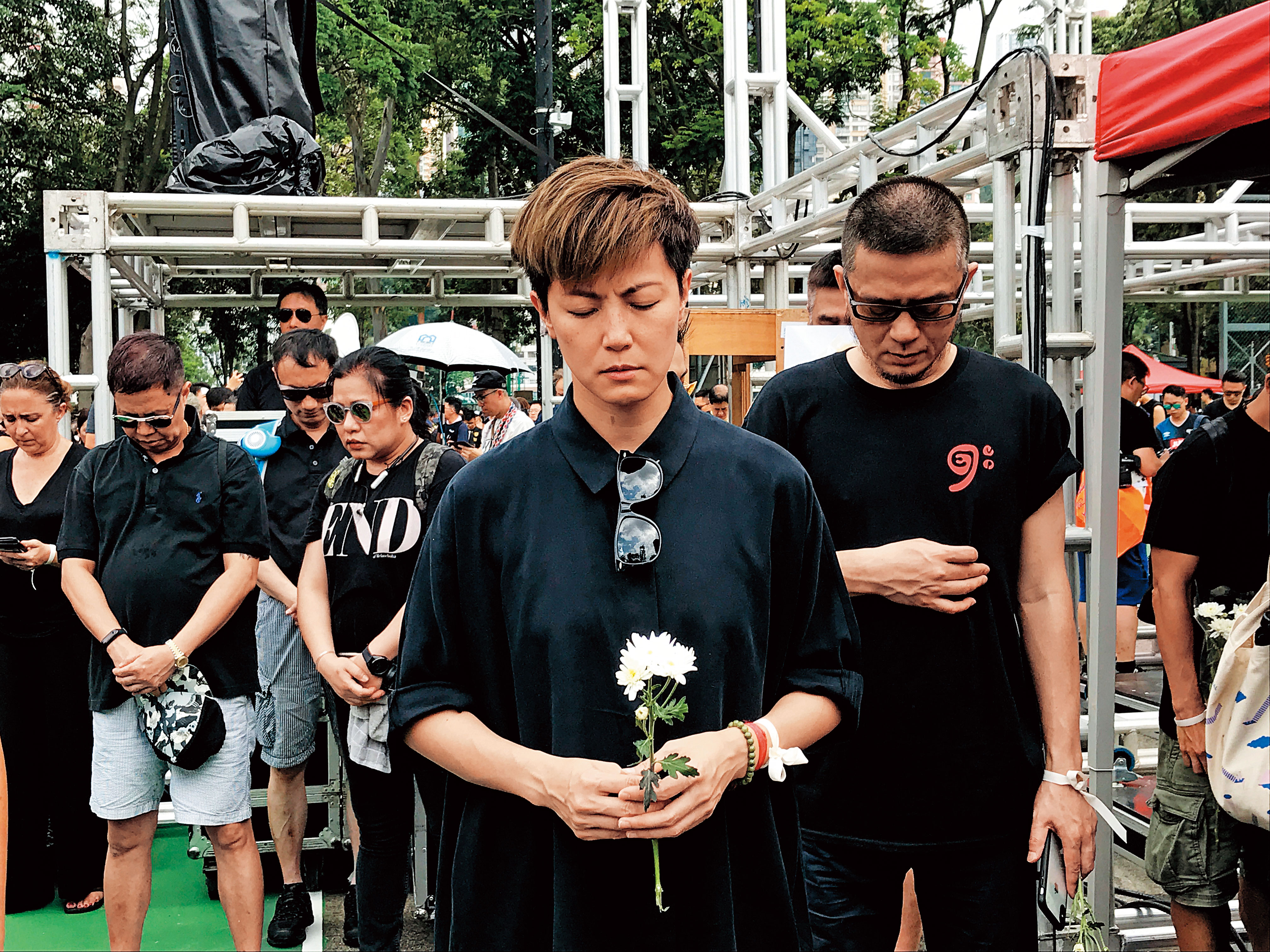 遊行起步前，民陣希望在場民眾為前日墜樓過世的抗爭者默哀，何韻詩手持白花、神情肅穆，右後為同樣勇於表態的藝人黃耀明。（陳怡靜攝）