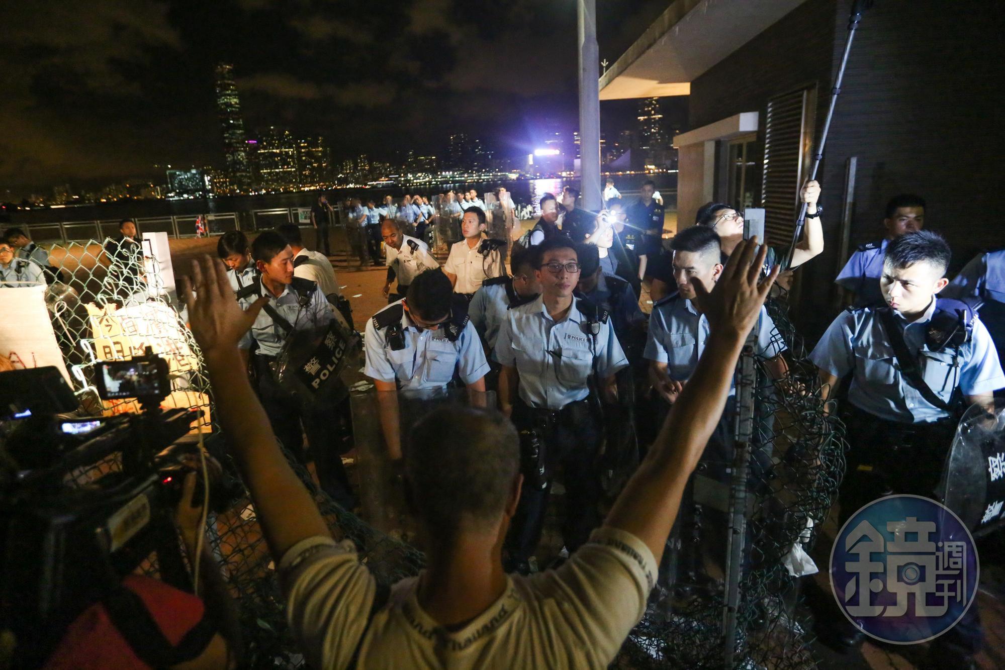 香港警察緊急加派警力駐守，一位示威者在鐵絲網外高舉雙手。