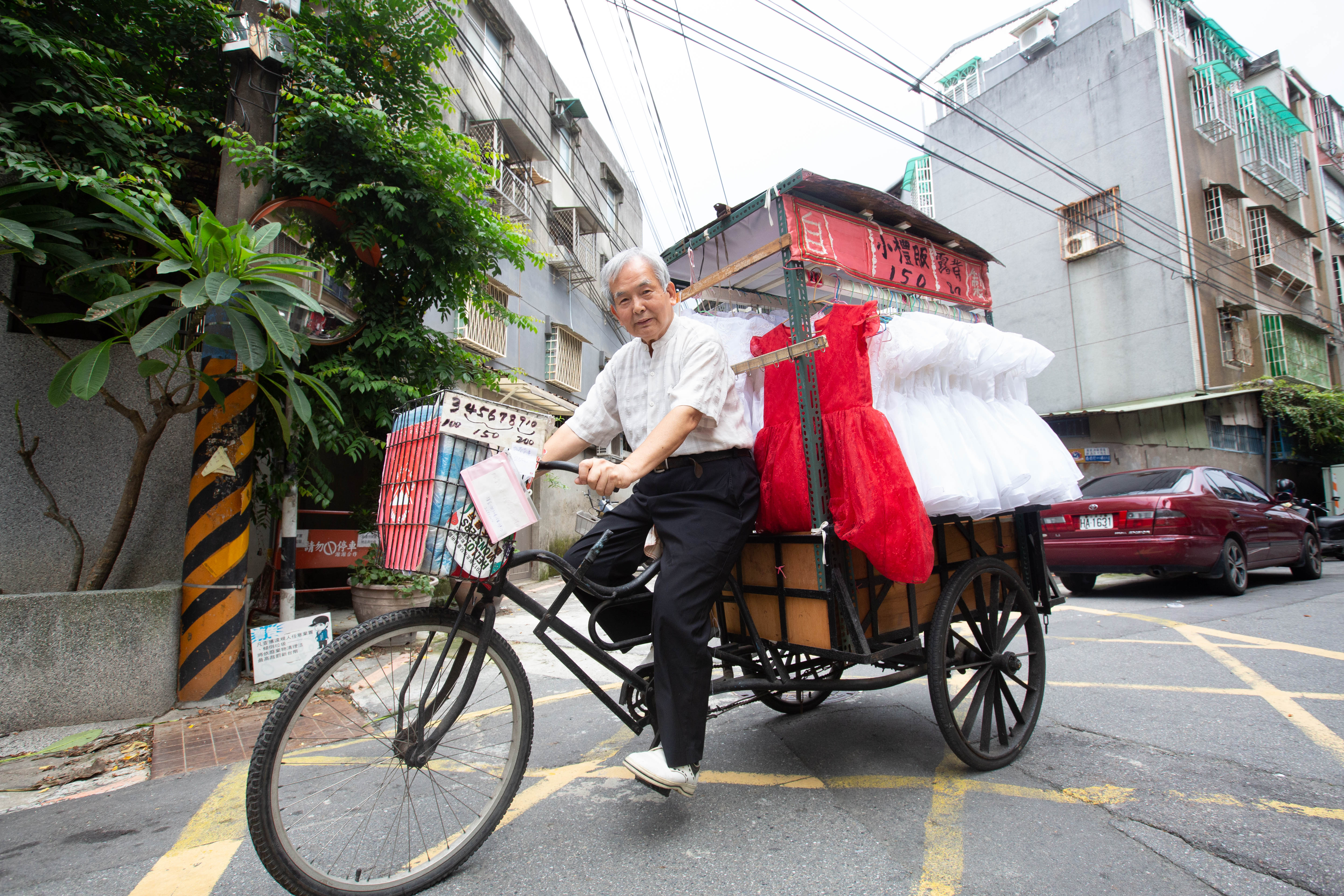 林哲慧以三輪車載著自己手作的小禮服已超過20年,圖中的紅色禮服是他做給孫女穿的