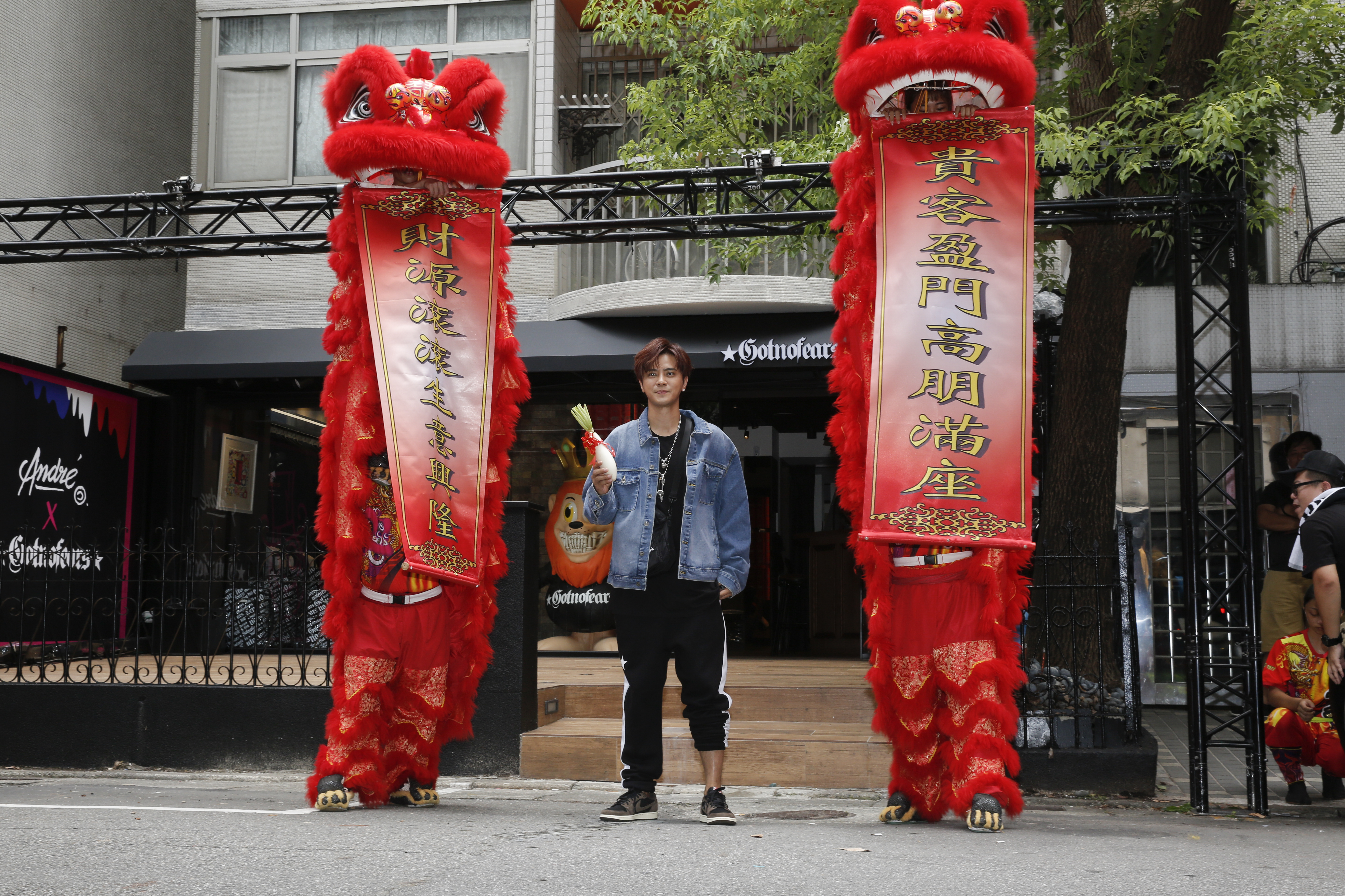 慶祝新店開張，羅志祥手拿象徵「好彩頭」的白蘿蔔，跟舞獅合影。請注意他左腳的褲款，這是故意捲上去的，不是他沒穿好，因為開幕活動他的造型都一直維持這樣沒變過。