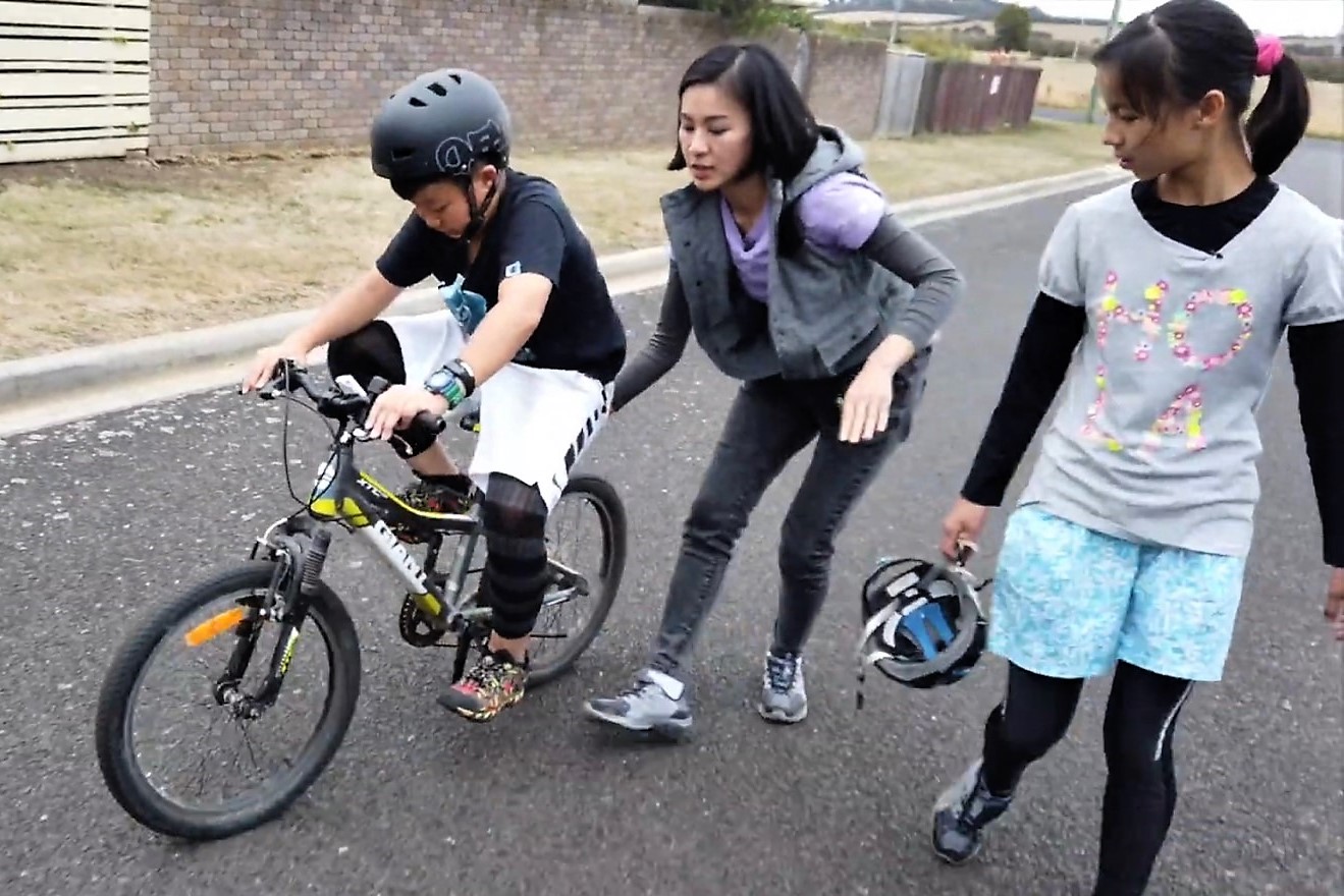 小小背包客可惟(左)在大家的鼓勵下決定挑戰學騎腳踏車,亞里(中)緊跟在旁協助。(公視提供)