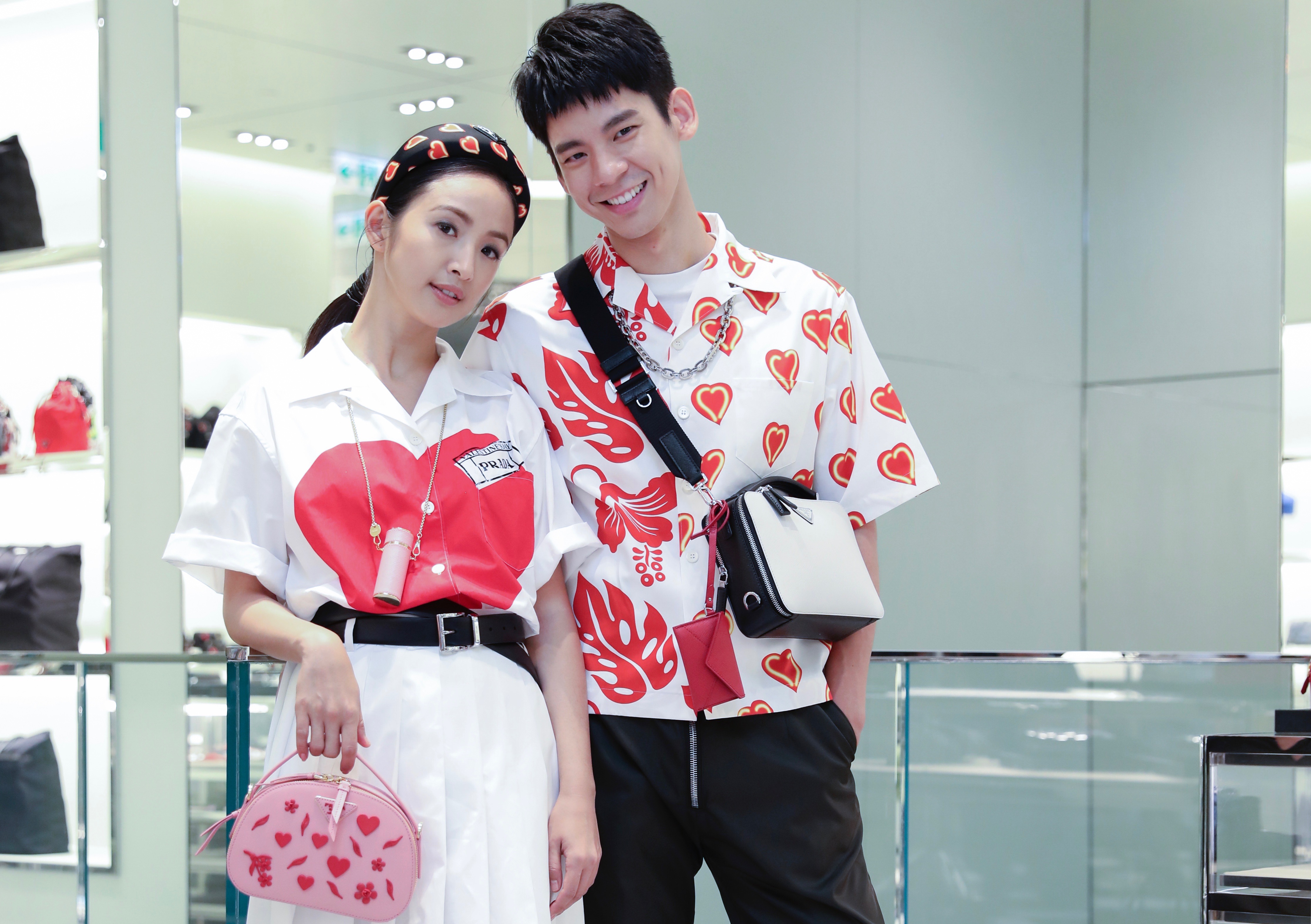 林依晨與林柏宏示範PRADA七夕情人節系列，林依晨脖子上掛的是一個小巧的口紅包，非常特別。林依晨：情人節系列愛心印花襯衫 NT$29,500、白色百褶裙 NT$40,500、手繪愛心圖紋髮箍 NT$8,000、Saffiano皮革鍊帶口紅包 NT$15,000、皮革腰帶 NT$14,000、情人節系列Odette手提肩背包 NT$76,000。林柏宏：情人節系列雙重印花襯衫 NT$36,000、黑色尼龍長褲 NT$36,000、多功能金屬鏈 NT$17,500、皮革腰帶 NT$15,000。