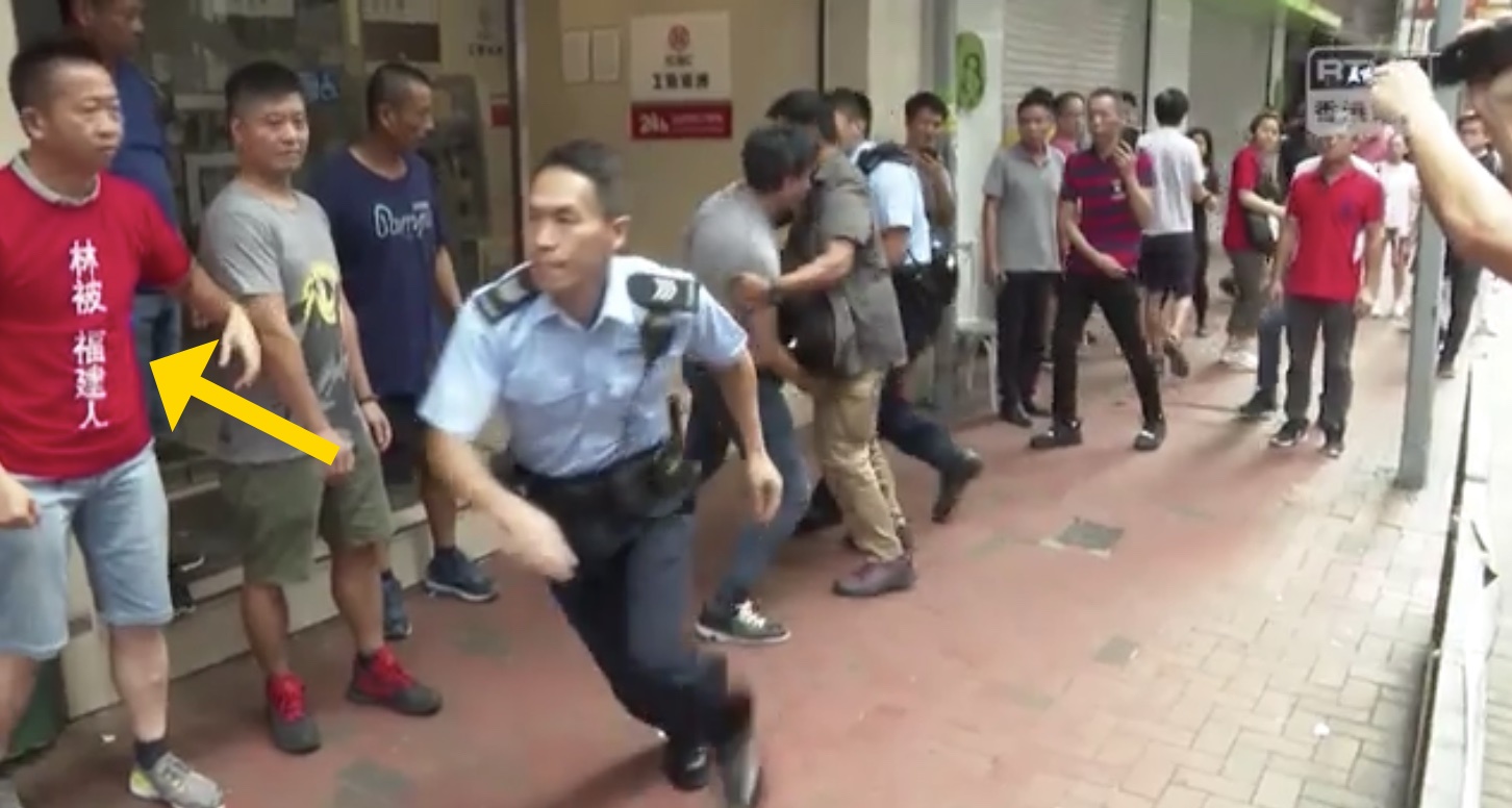 北角警察跑去抓人，身旁一位紅衣人，衣服上頭有「林被 福建人」的字眼。（翻攝自RTHK）
