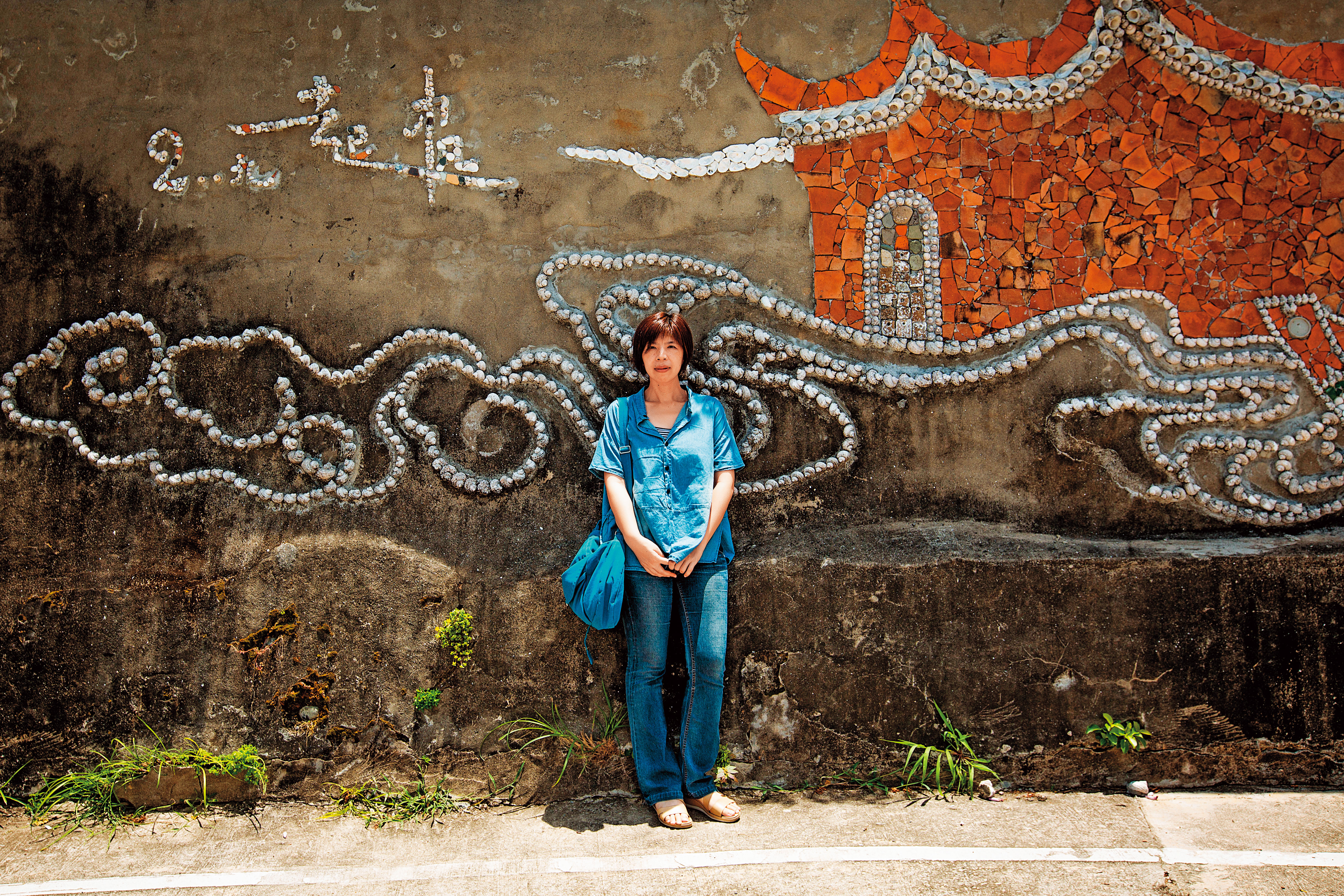 廖億美是整個大浦聚落活化的形塑者。她背後的拼貼壁畫，由她邀請的藝術家蔡英傑利用在地素材所完成。