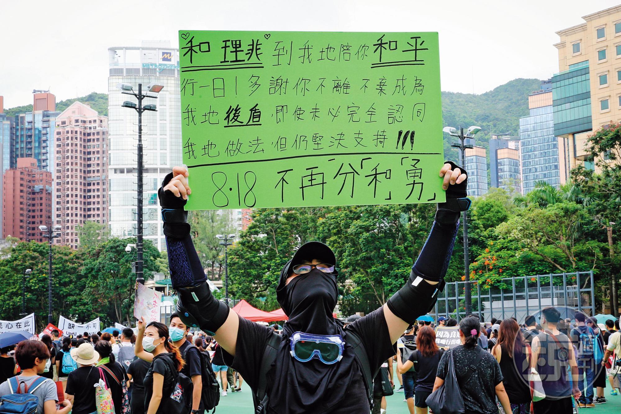 威爾(化名)高舉自備手寫看板,主張「818不再分『和』『勇』」,頂著高溫,在維園的一角苦站。