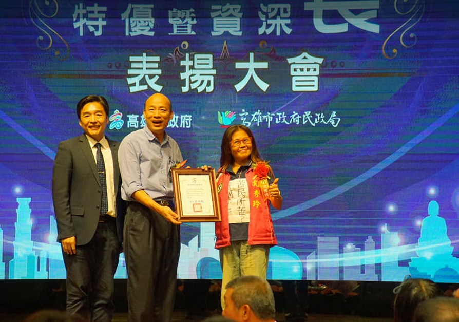 正興里里長沈秀玲身貼「苦民所苦？睡到中午！」的紙條上台嗆高雄市長韓國瑜。（翻攝正興里里長沈秀玲服務處臉書）