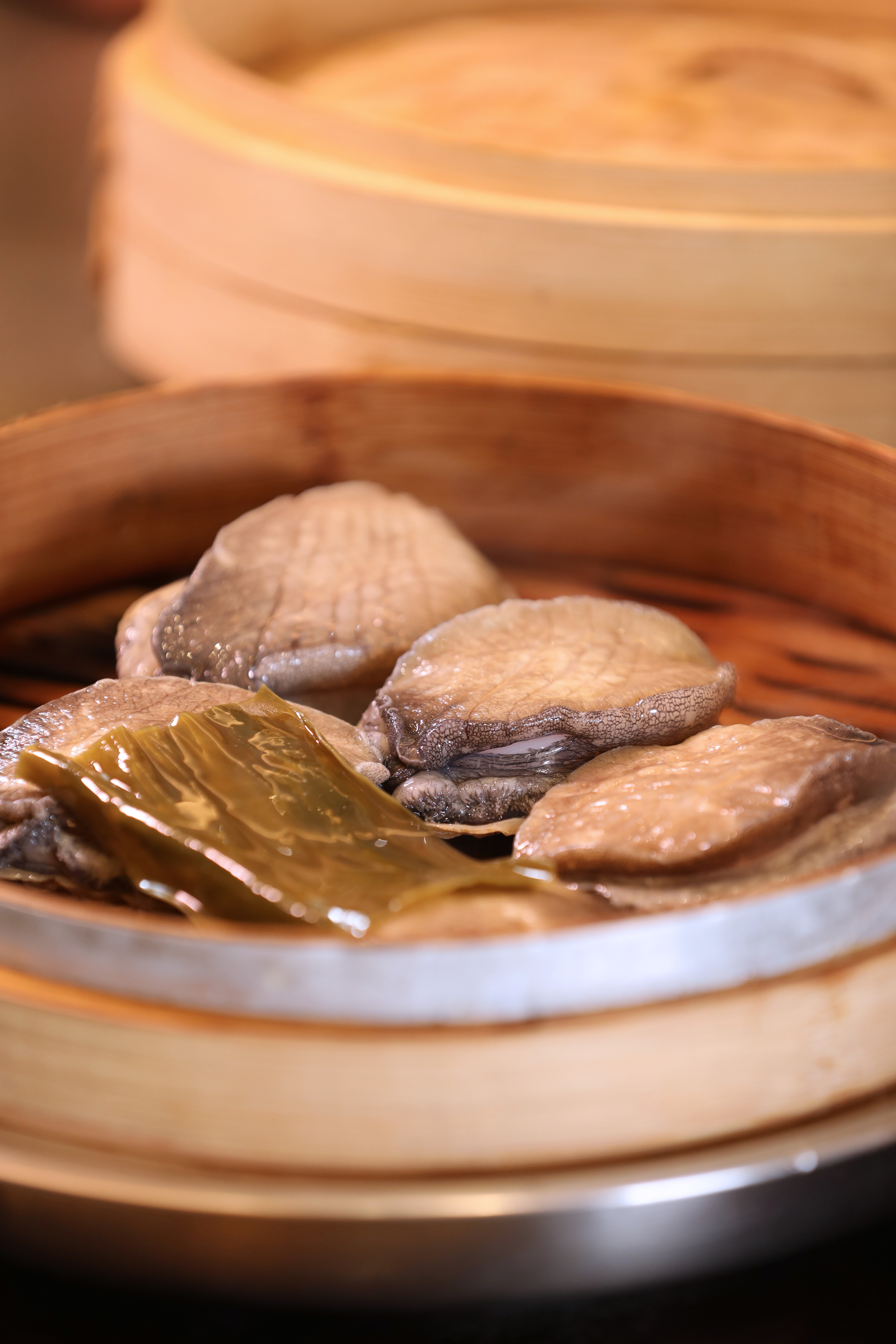 將竹蒸籠搬上鐵板，在客人面前現蒸鮑魚。