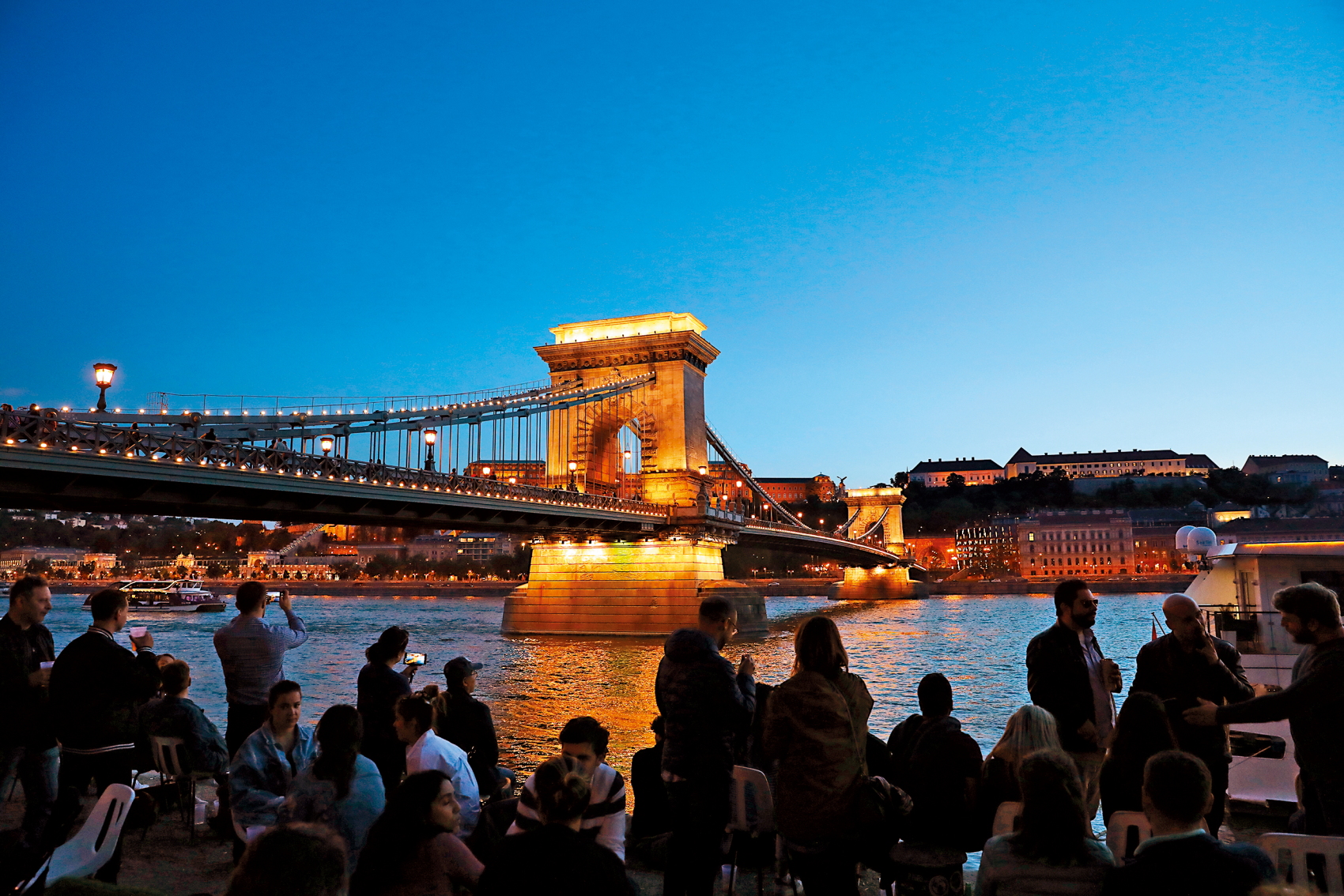 夜間亮起燈光的鏈橋，吸引許多遊客在河岸邊欣賞。