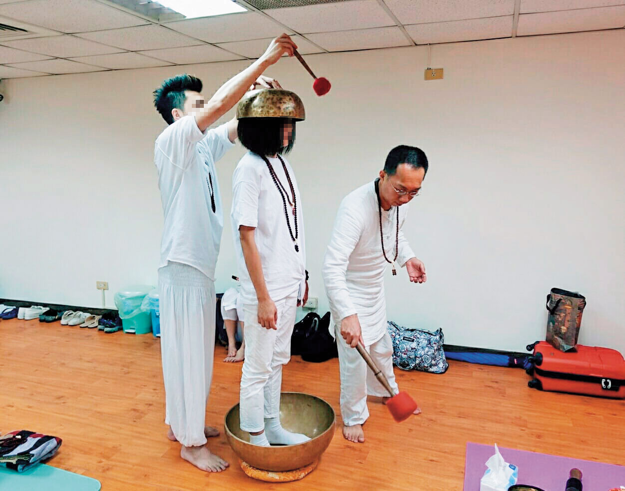 許台融(右)將大缽放在學員頭頂與腳下敲擊,聲稱發出的音波能和人體產生共鳴。(翻攝臉書)