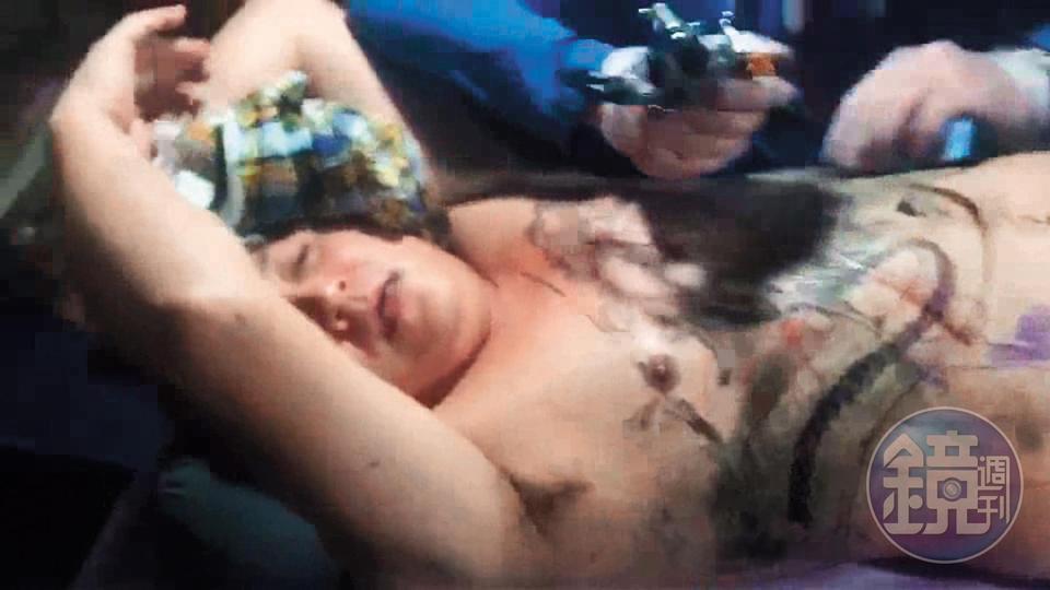 關於「紋身入黑道」，有段影片高盟傑打著赤膊、仰躺向上，雙手抱頭並且嘴巴咬著衣服，似在忍痛刺青。（讀者提供）