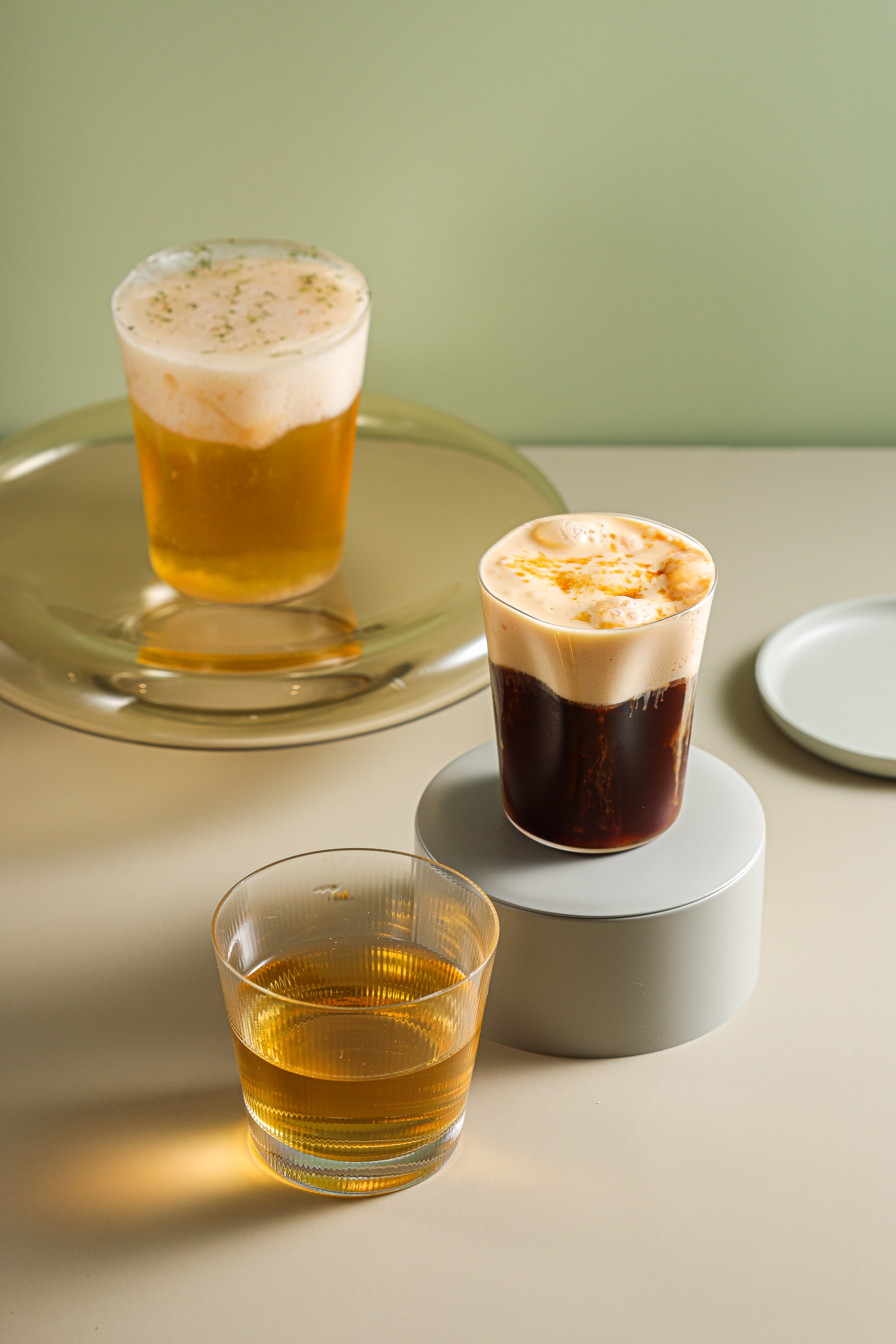 「Honey Shakerato」（中）在哥倫比亞冰咖啡擠上溫熱焦糖慕斯，口感冰溫交錯。江振誠很喜歡的「Momotaro」（後），以阿里山烏龍茶疊上水蜜桃慕斯、薄荷櫻花碎冰，喝之前要先敲破碎冰，沁涼清爽。（皆180元／杯）