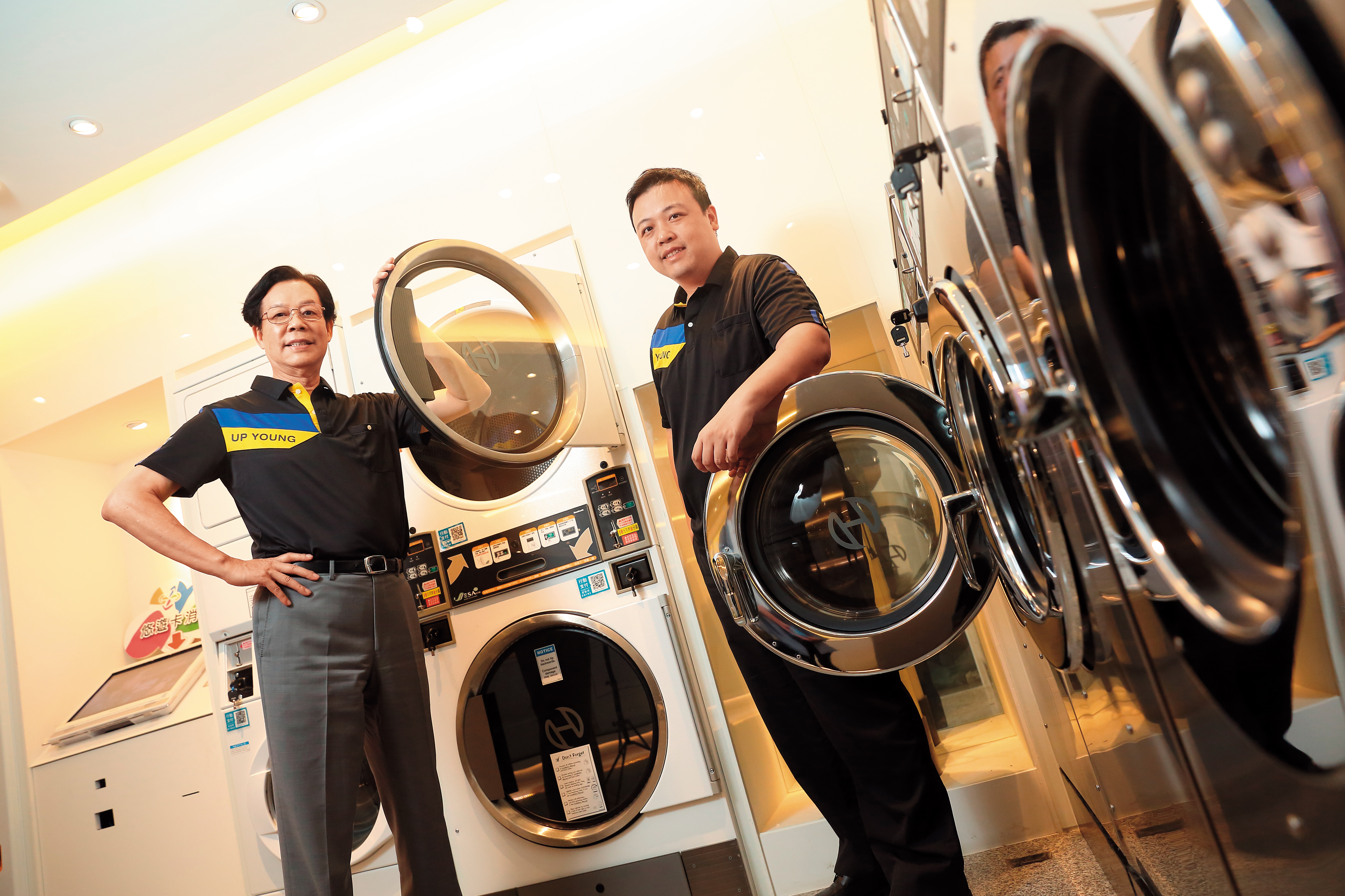 吳明富（左）40年前棄公職創上洋產業，全台首創自助洗衣店，積極打入大專院校、醫院。兒子吳國華（右）接棒拓展代理美日家電品牌，穩坐商用自助洗衣龍頭。