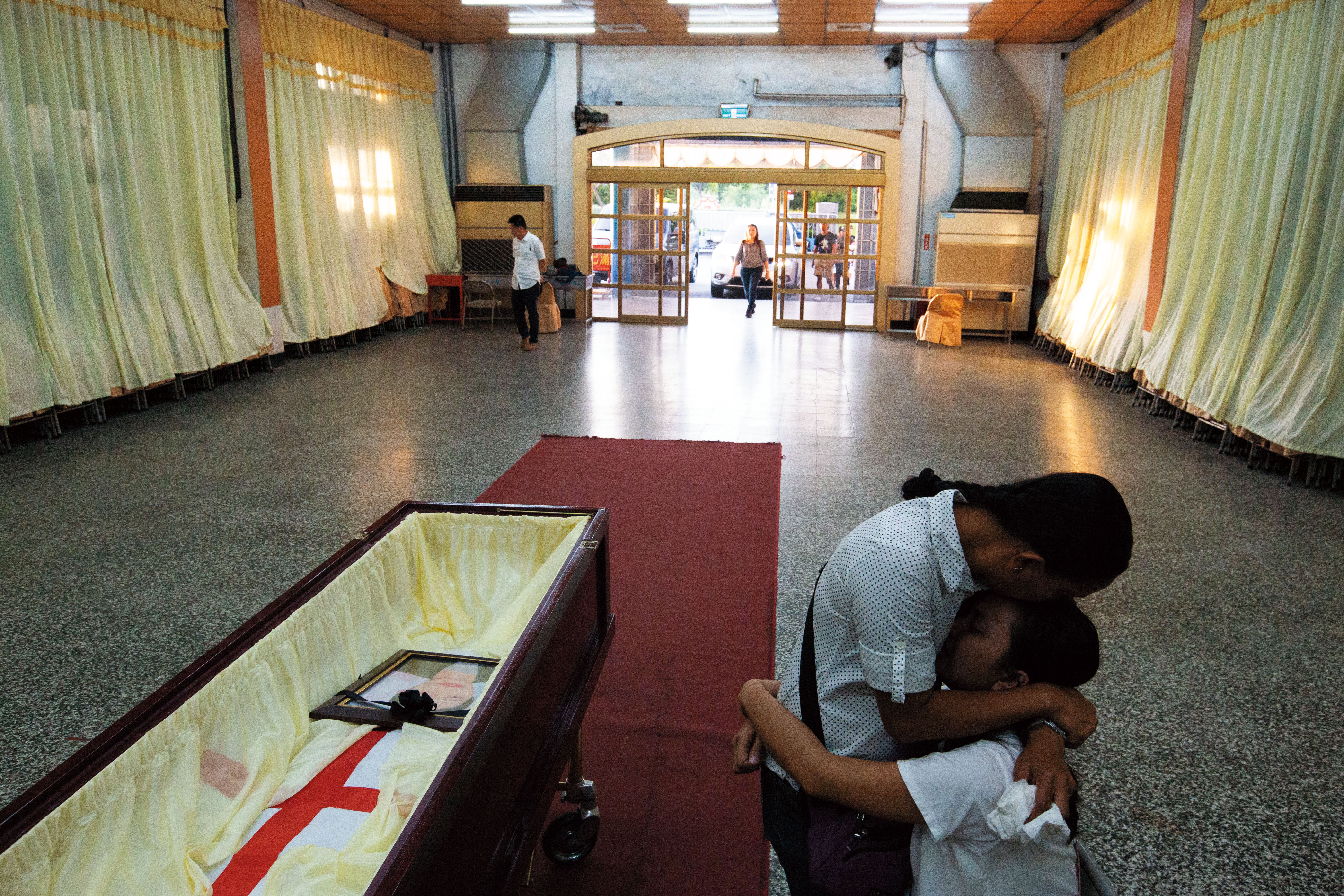 德希莉的遺體未火化，完整送回故鄉，三姊德娜（左）、七妹德琪（右）在棺木旁相擁痛哭。