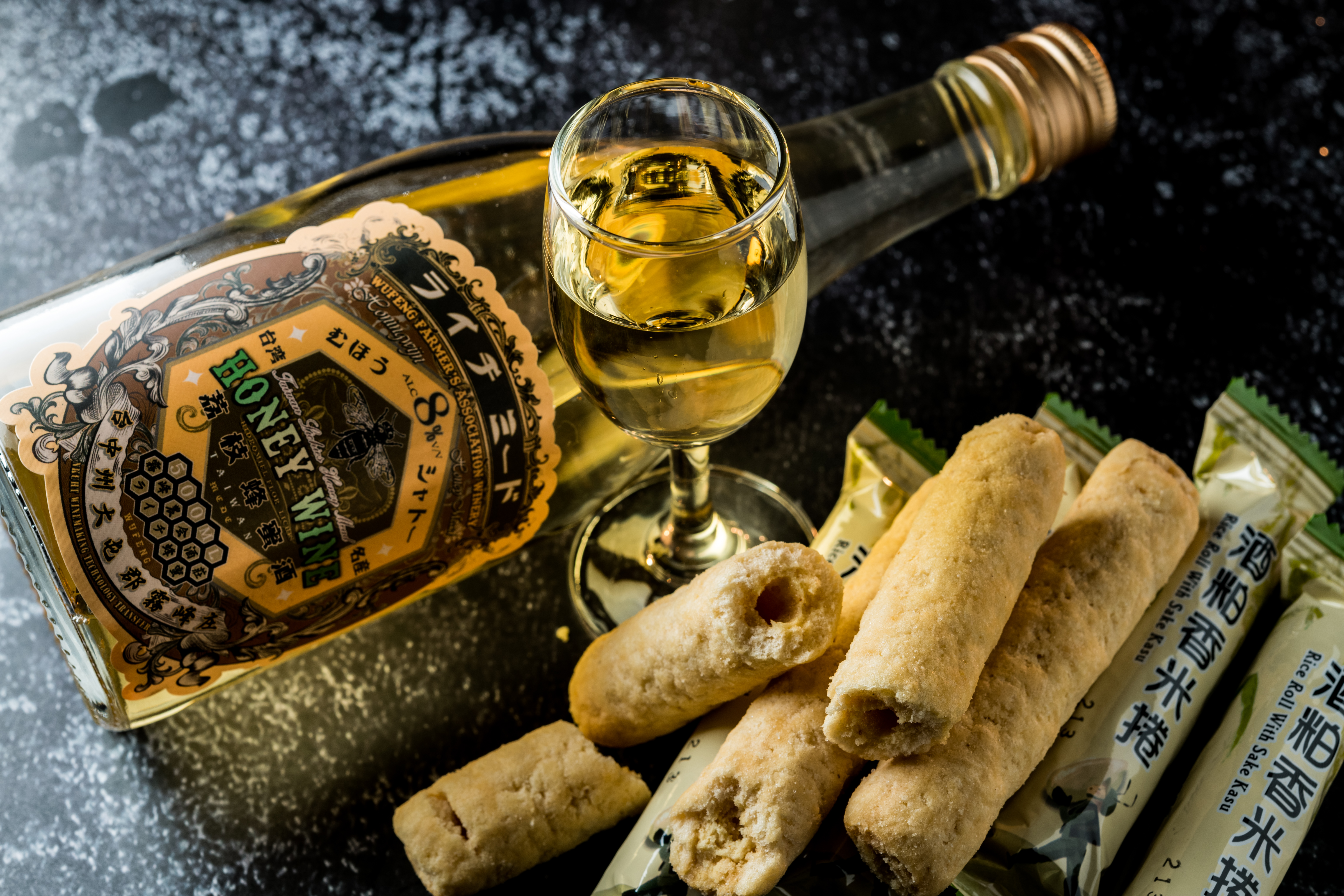 「荔枝蜂蜜酒」（左，680元／瓶）用霧峰在地農產荔枝汁為主原料，釀製輕甜蜜香，風味討喜，搭以酒粕與益全香米製成、香Q的「酒粕香米捲」（右，120元／袋）也不違和。