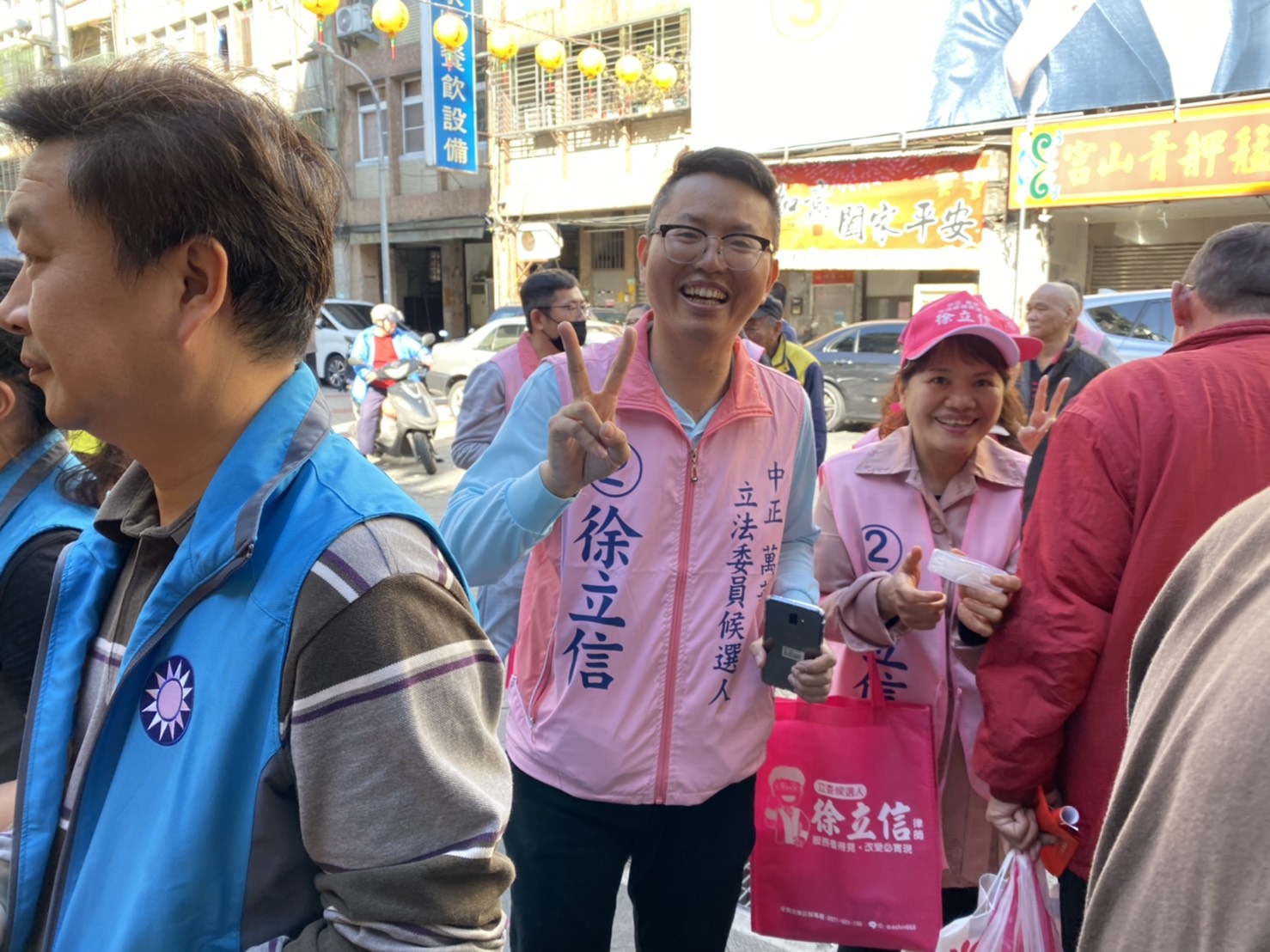民眾黨的徐立信被藍營眾多的支持者卡在角落，只能無奈比出手勢苦笑。（讀者提供）