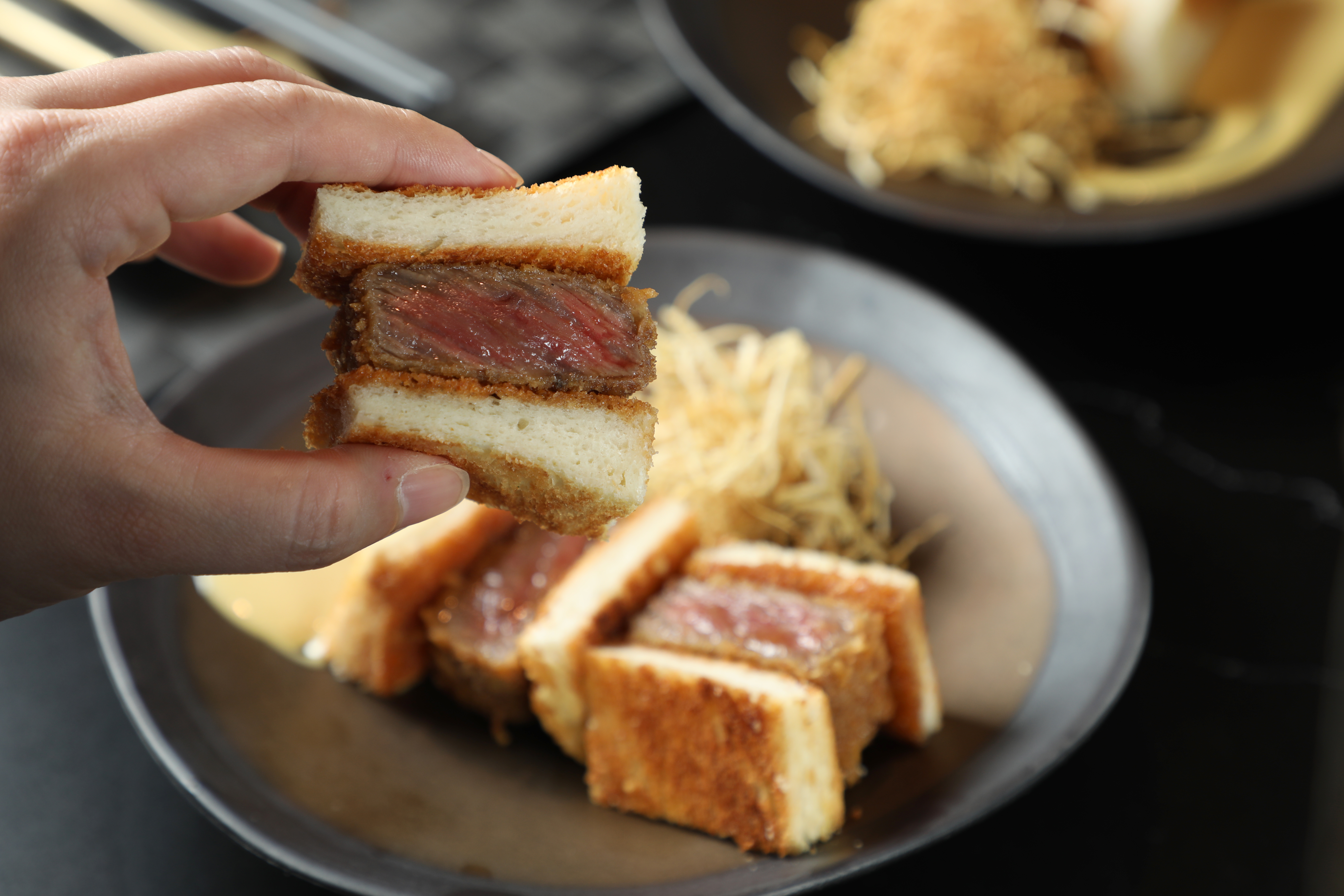 用拇指、食指掐起「A5和牛牛排三明治」，一口咬下，脆、潤、彈多種口感在嘴裡綻放。（搭配1,280元起牛割烹套餐，加價680元／份、單點780元／份）