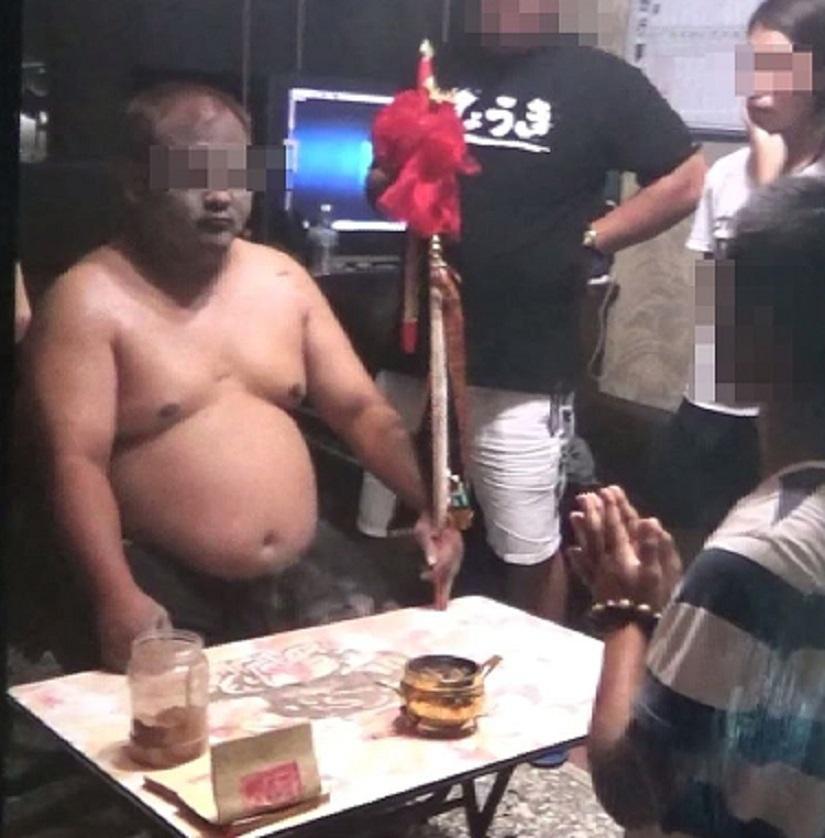 神棍陳兄作法事，郭女在旁隨侍，與弟弟郭男跪在案前。（翻攝畫面）