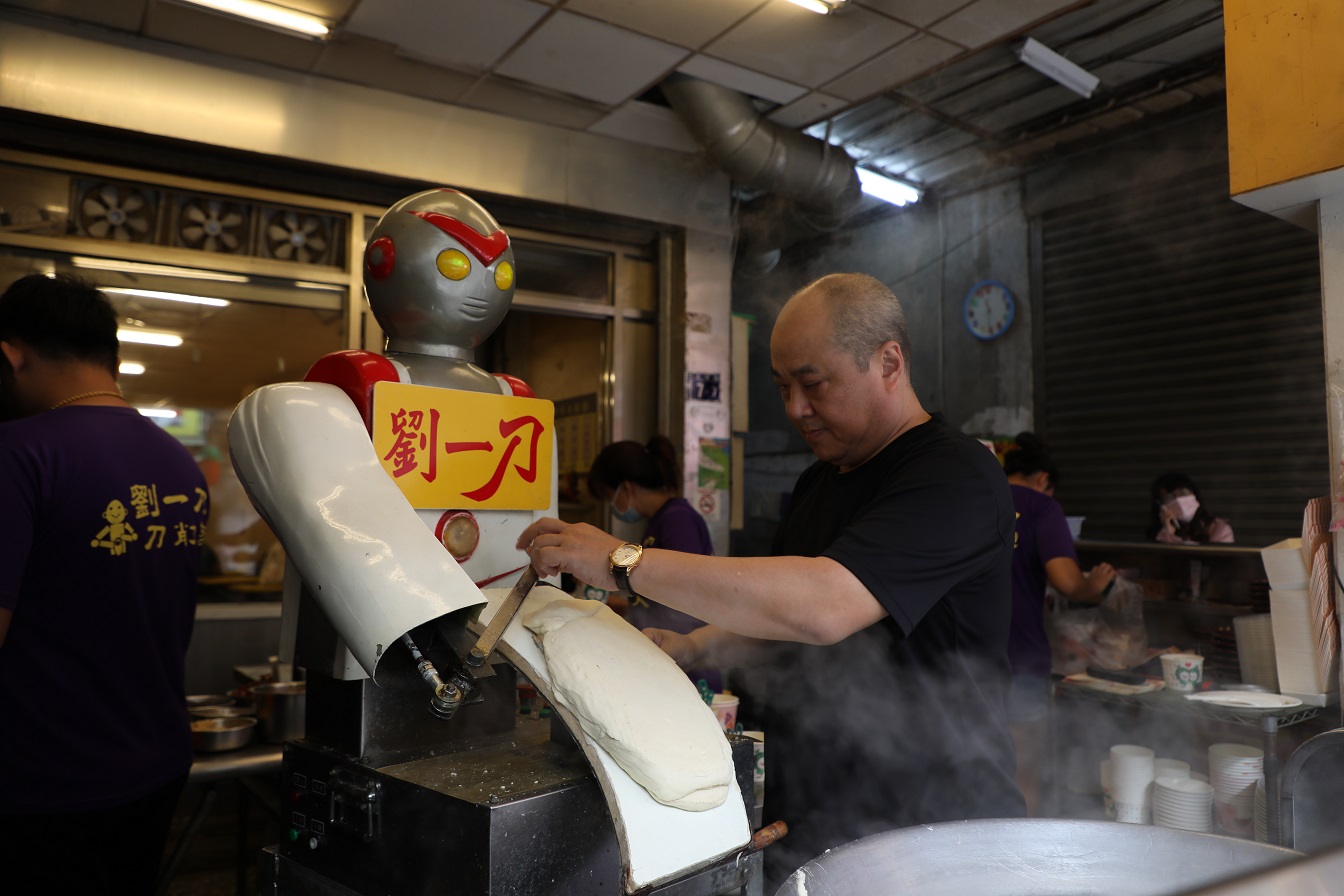 店主劉彥慶在機器人前面放上麵團。
