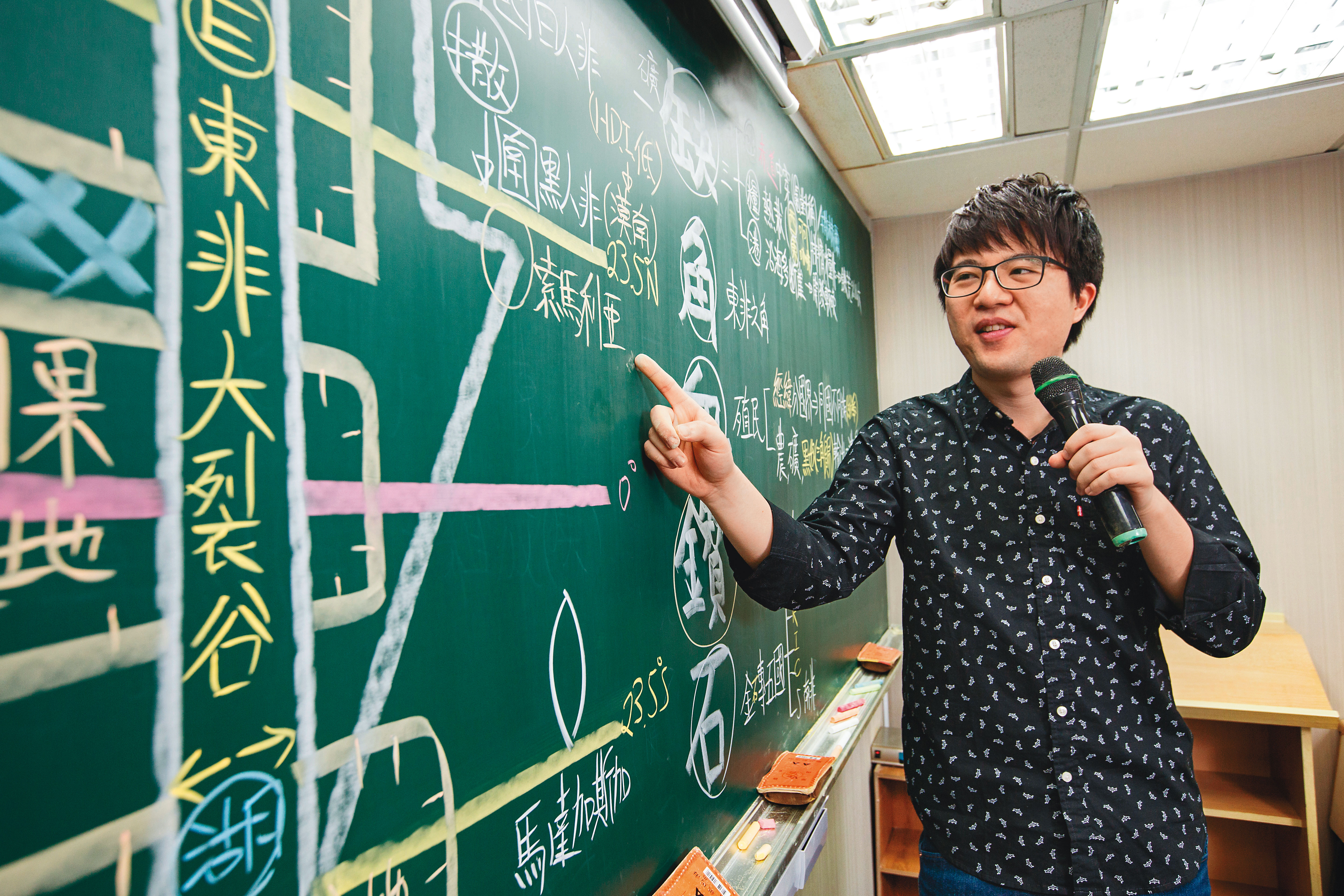 補教地理名師劉成霖在講台上畫地圖以及教學生地理知識，而他另一身分則是投資達人。