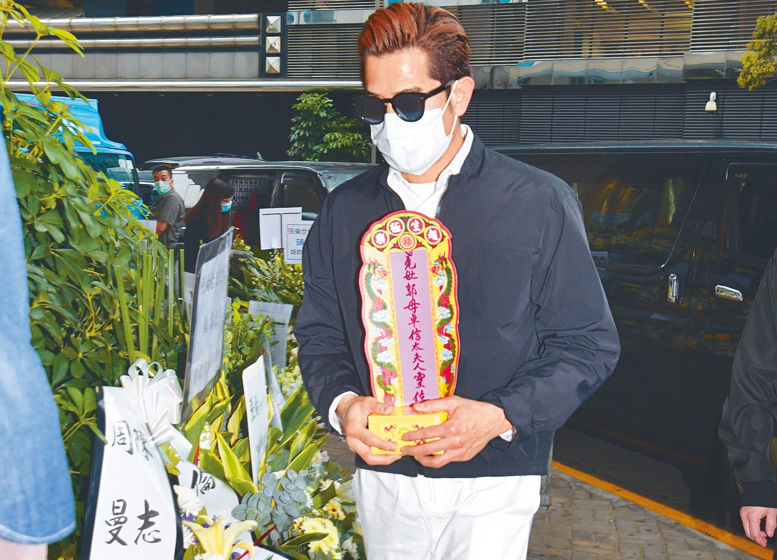 身穿孝服及黑色外套的郭富城戴上墨鏡及口罩，雙手捧着亡母的靈牌步入殯儀館。（東方IC）