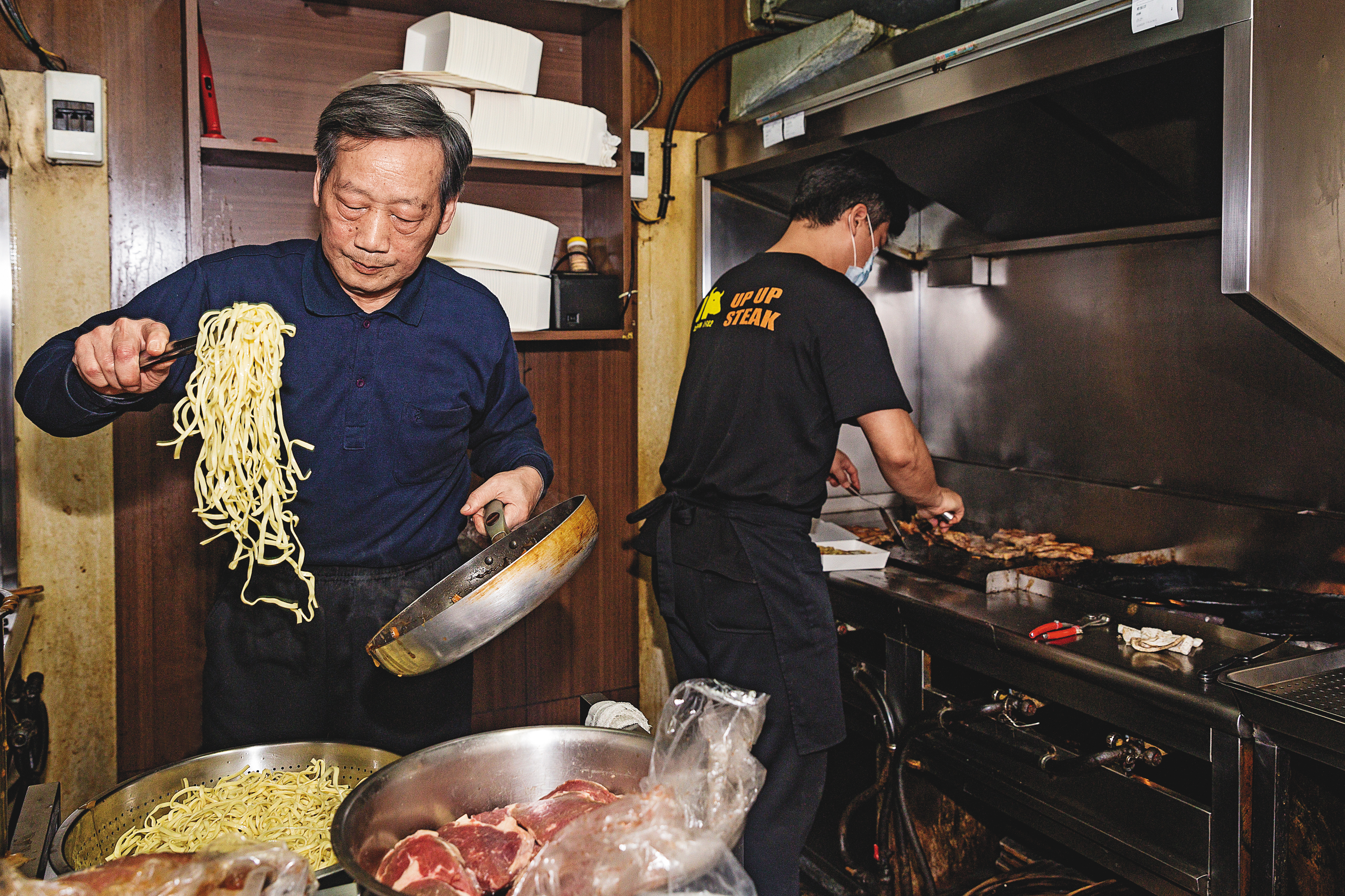 煎了大半輩子牛排,江鴻烈(左)退而不休。今年64歲的他,每天仍準時到店裡坐鎮。江旻軒(右)在另個煎檯,以不到2分鐘的速度,熟練地完成7分熟牛排。
