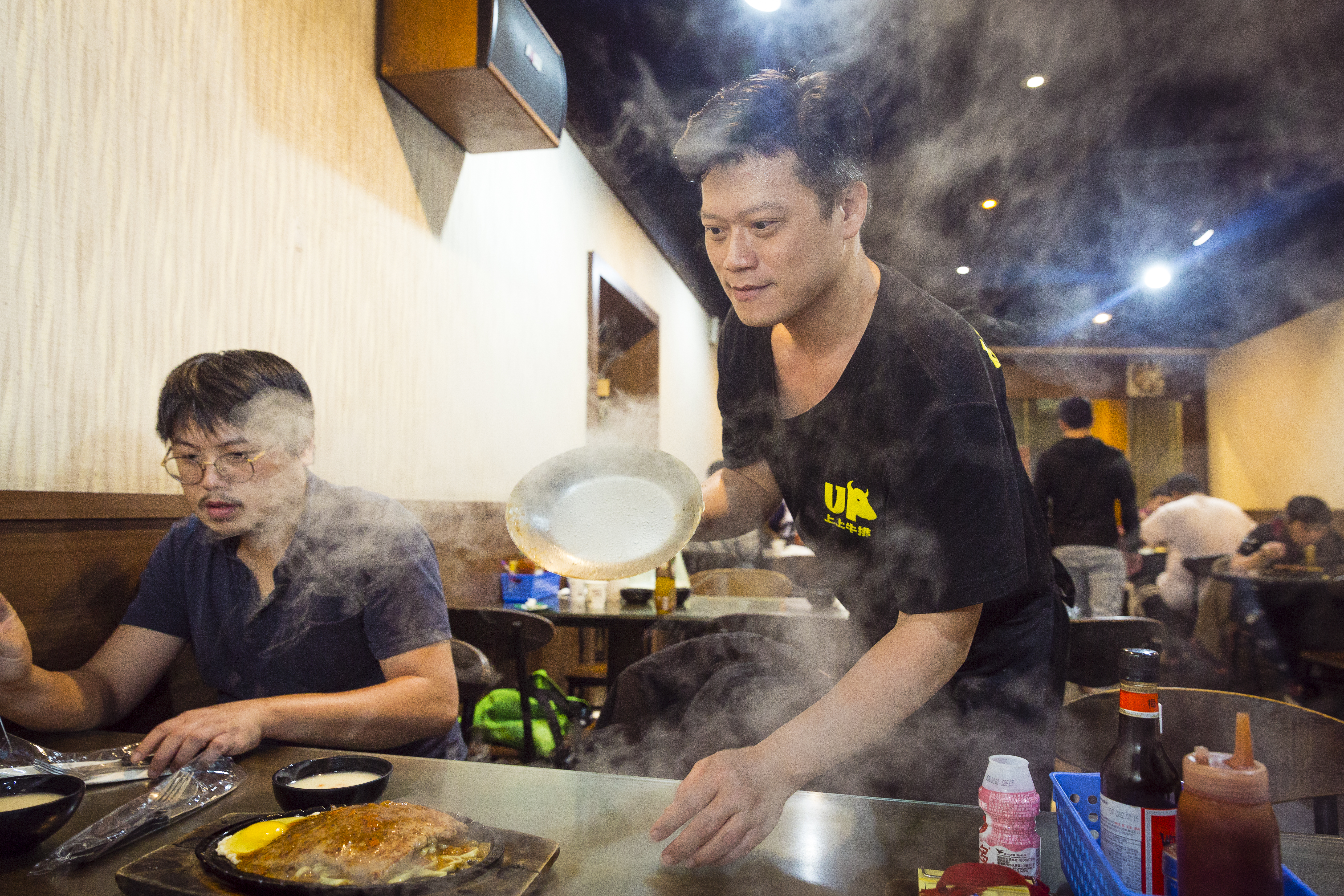 平日晚上六點不到，店內也已近滿座。江旻軒把蓋子一掀，黑胡椒牛排的香味和著煙一起衝出。