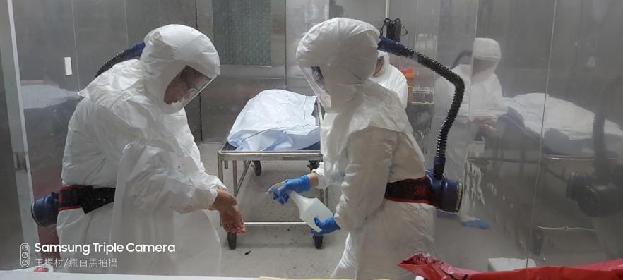 解剖法醫、助手穿戴正壓呼吸器，相互協助消毒，不容成為防疫破口。（法務部法醫所提供）