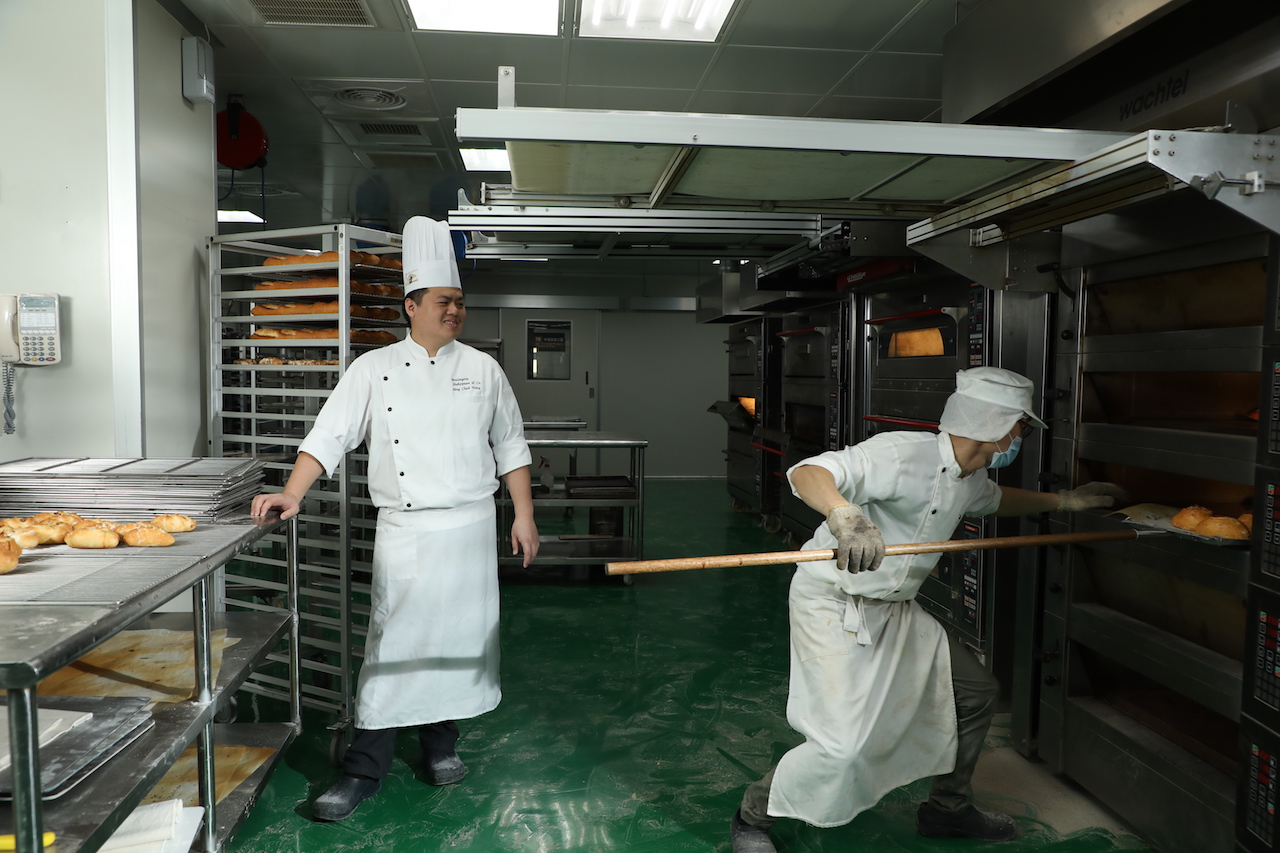 中央廚房裡工作人員忙著整形麵糰、烤焙麵包，動線及分工分明。