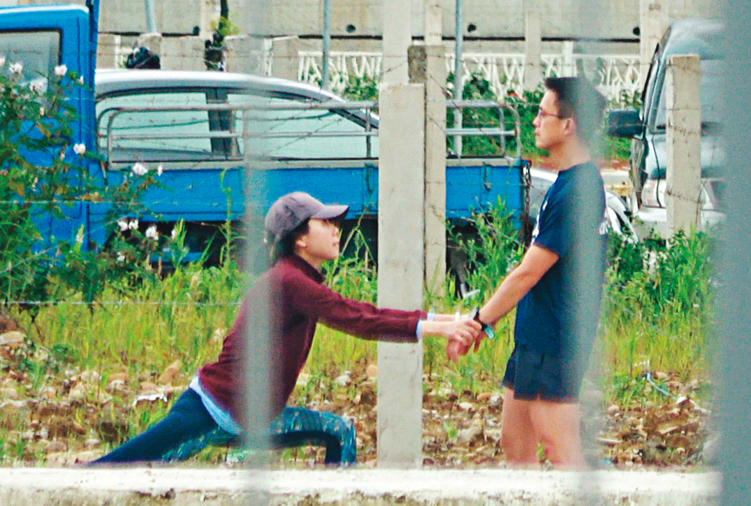  4/25  12 : 49，跑步前，吳彭弘（右）跟簡芳貞（左）先在路邊拉筋，2人拉著雙手，簡蹲下伸展下肢，整體看起來滑稽。