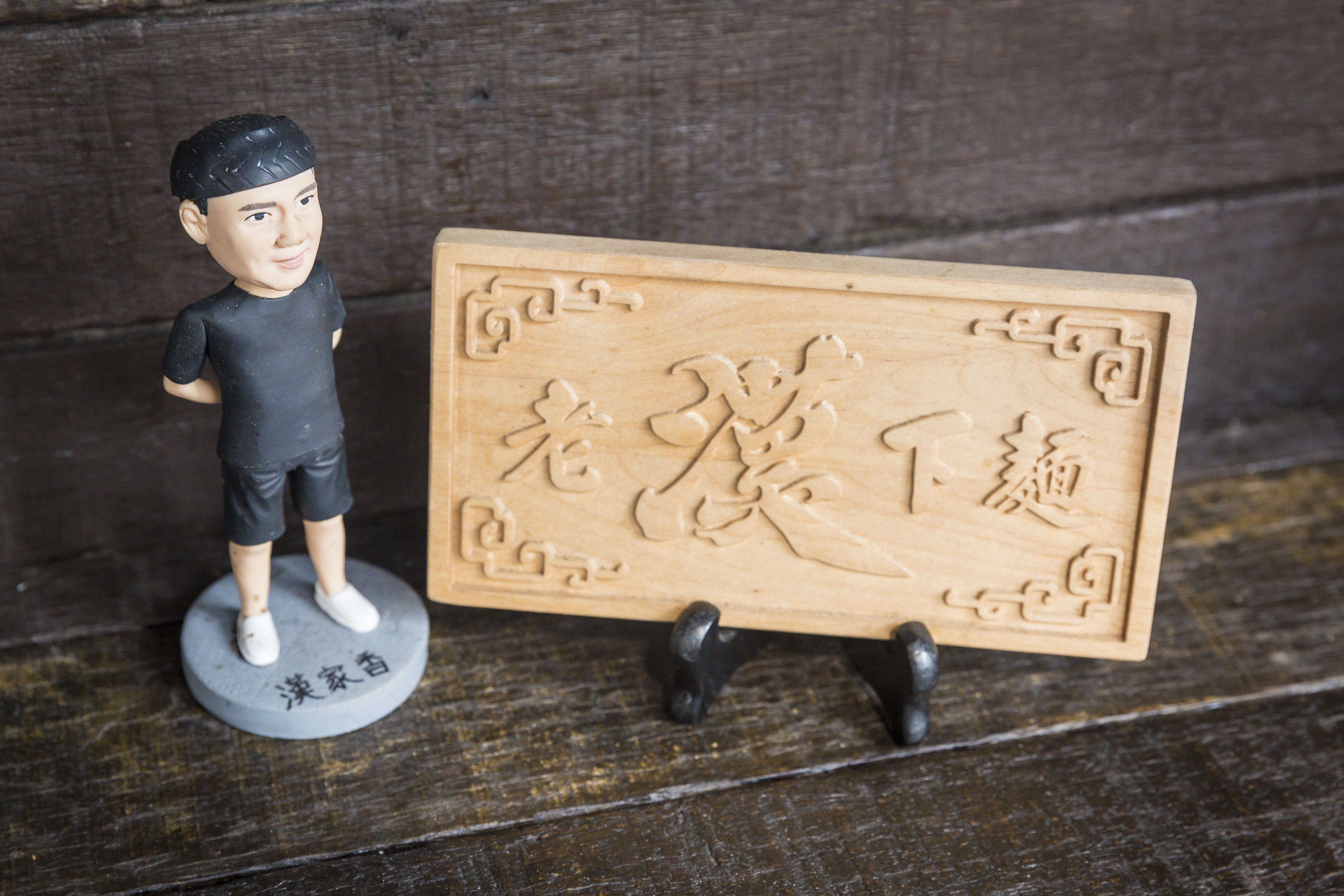 去年開實體店面時，監獄管理員送他一個「老漢下麵」迷你匾額。就擺在店裡長桌一角。