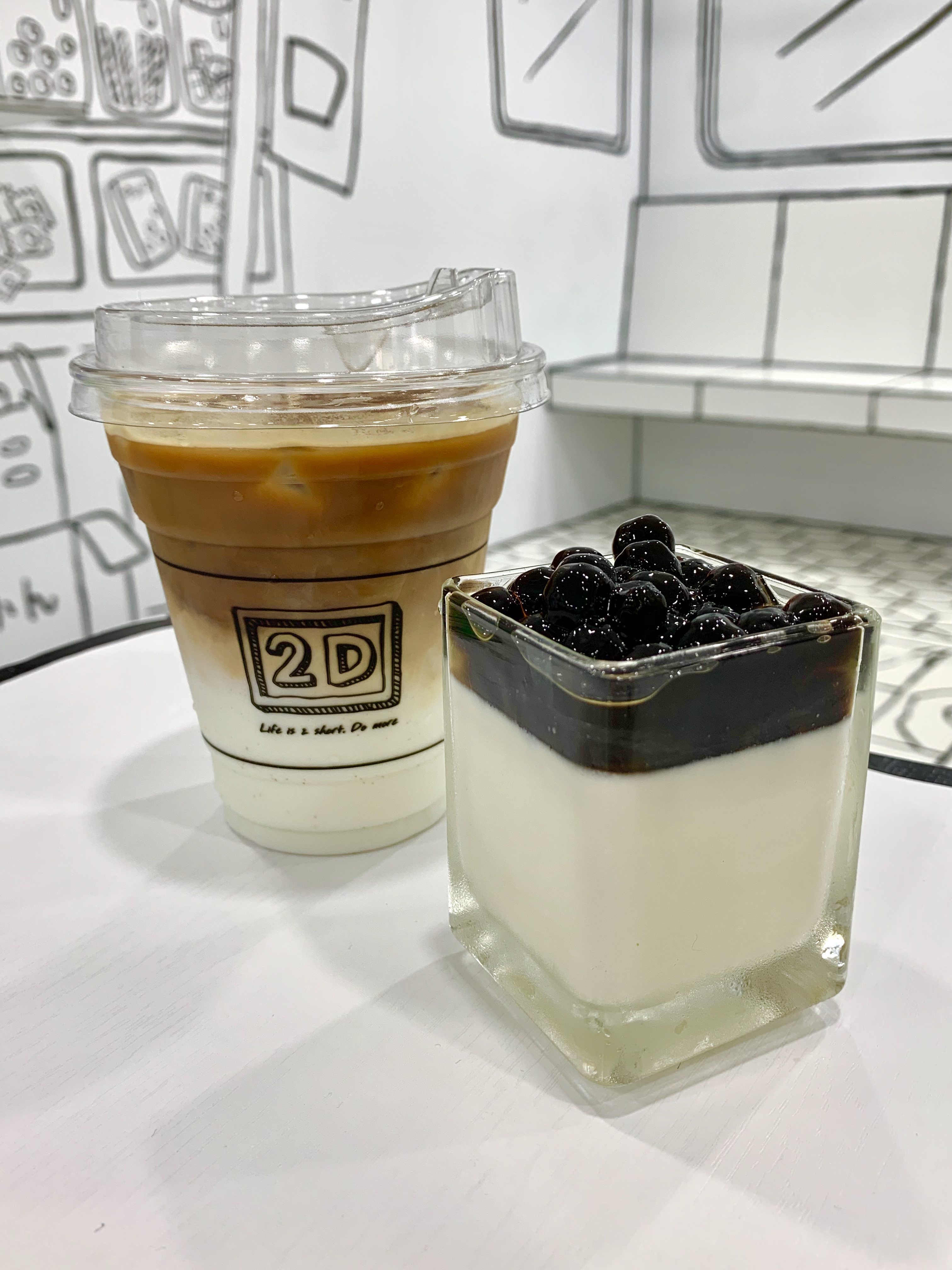 刻意做漸層色的「2D招牌拿鐵」（後，130元／杯），苦韻重了些，拌勻牛奶較好入喉；「鮮濃奶酪」（前，80元／份）珍珠有蜂蜜的甜香味，奶酪上層口感較為稀水，下層比較濃綿。