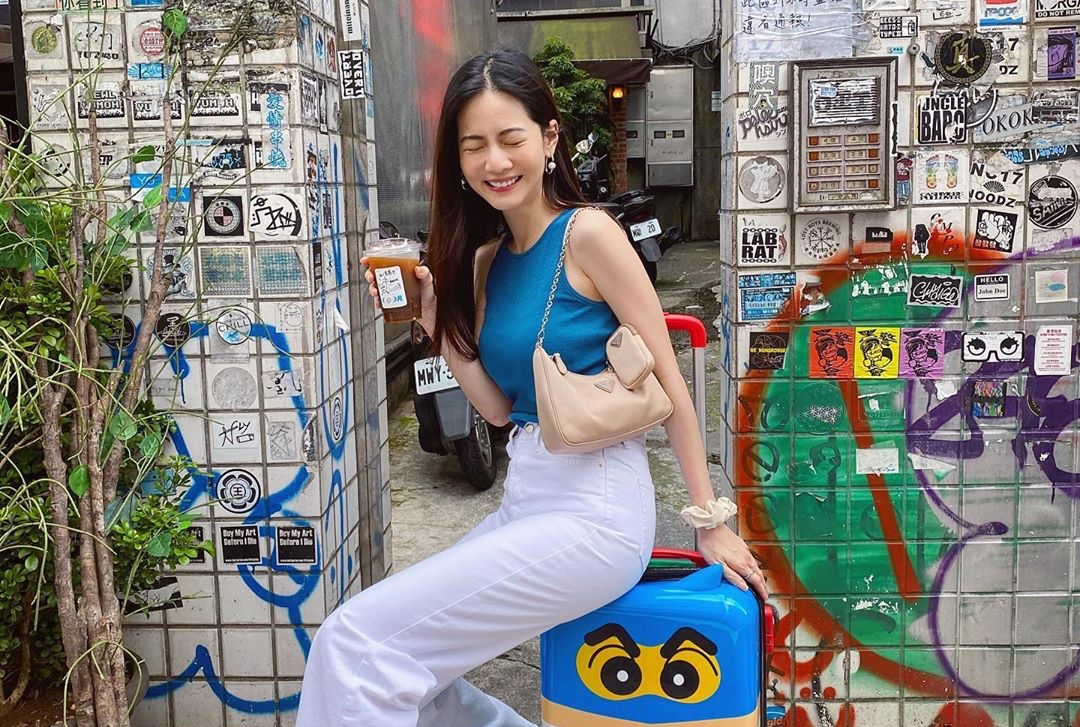 曾之喬笑瞇了眼睛，背著PRADA尼龍肩背包坐在行李箱上，暑氣褪散神清氣爽。（翻攝自曾之喬IG）