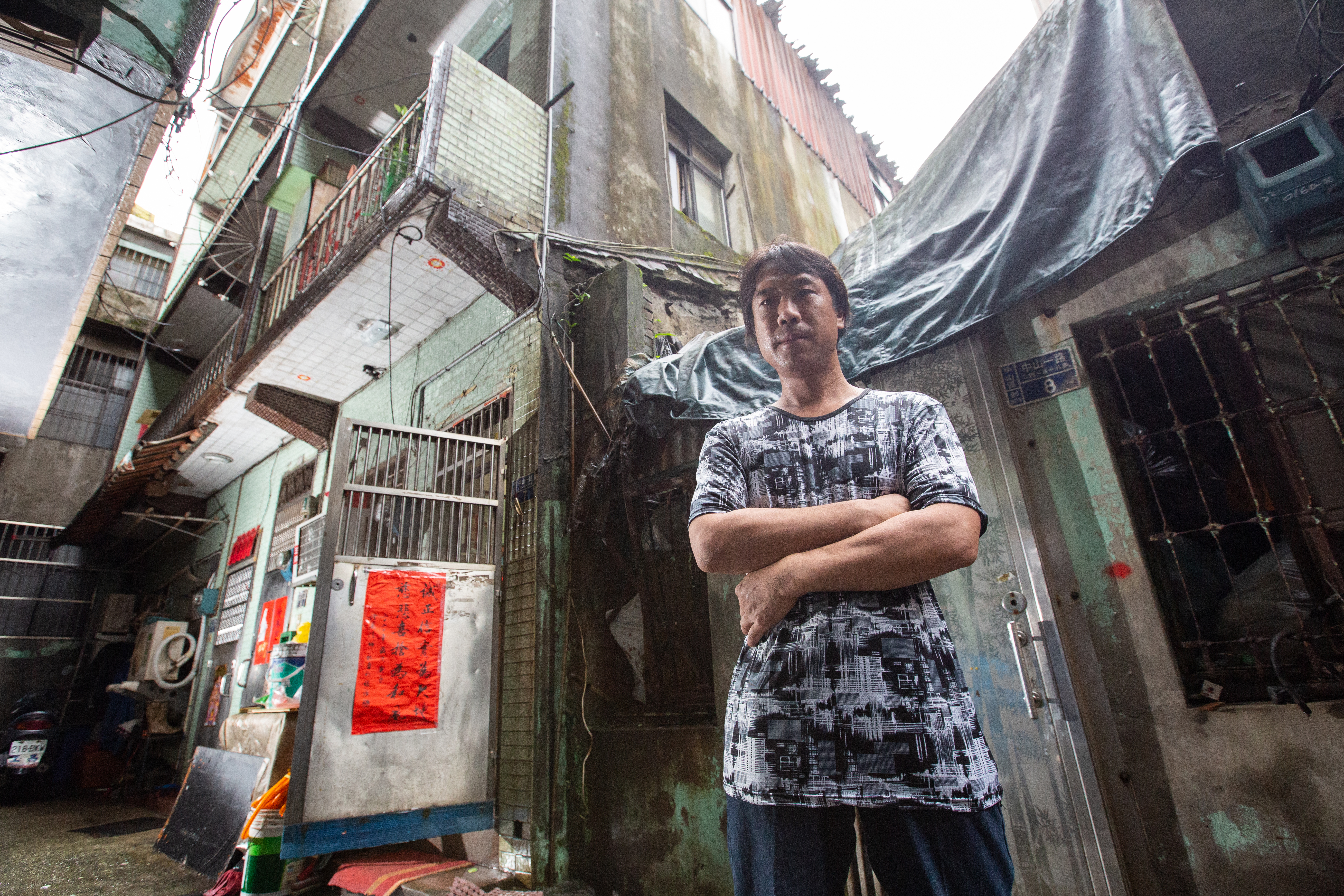 陳青旭身後的3樓透天厝，雖然潮溼老舊，卻是一家6口的家，因為欠繳1萬8千元的交通罰單，家差點不見了。