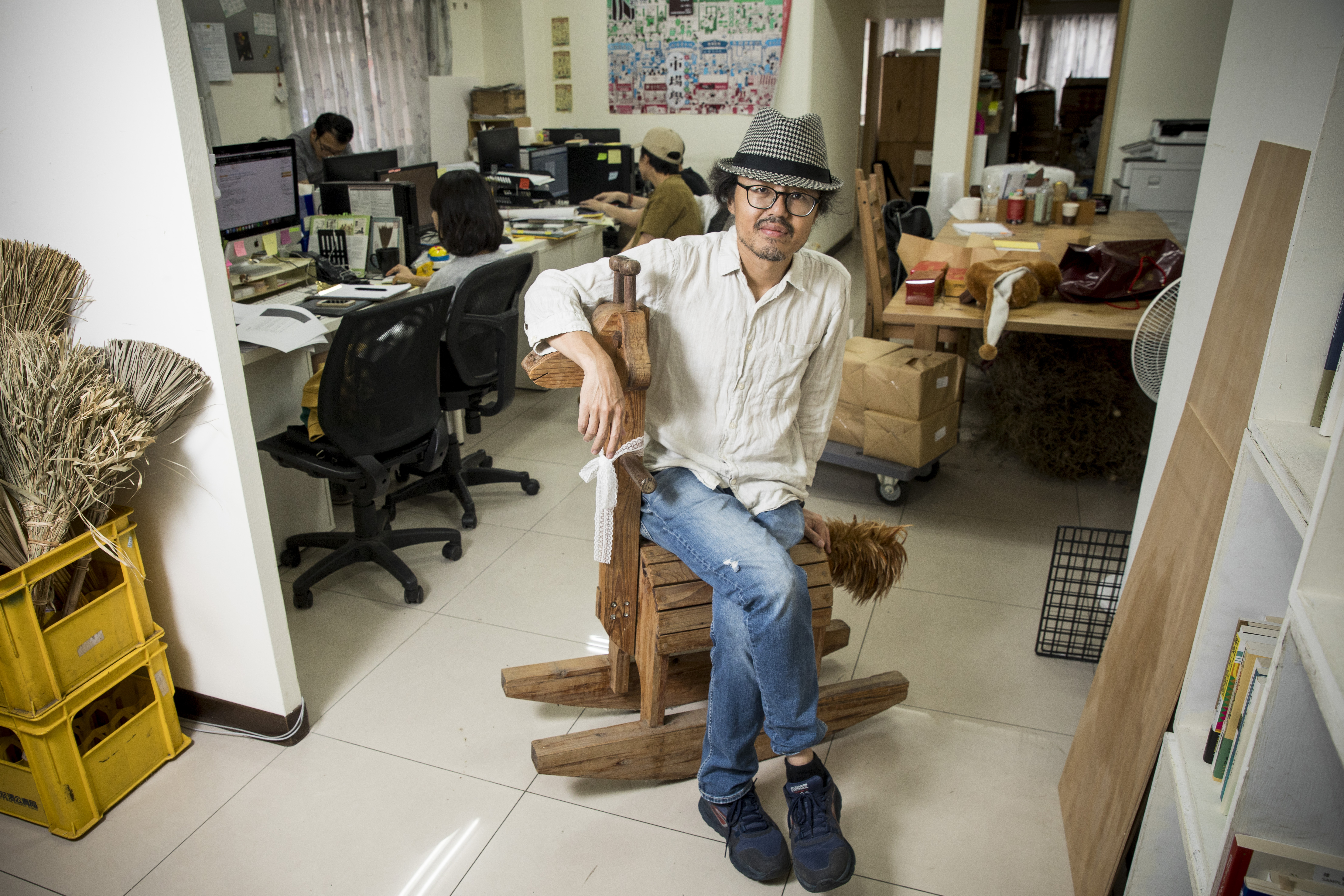 周易正在辦公室裡。左邊的掃把是去年底的公司企畫，搜集台灣各地用不同材料、技藝做出來的掃把，本來想辦展，但因疫情暫緩，目前僅有年曆周邊。